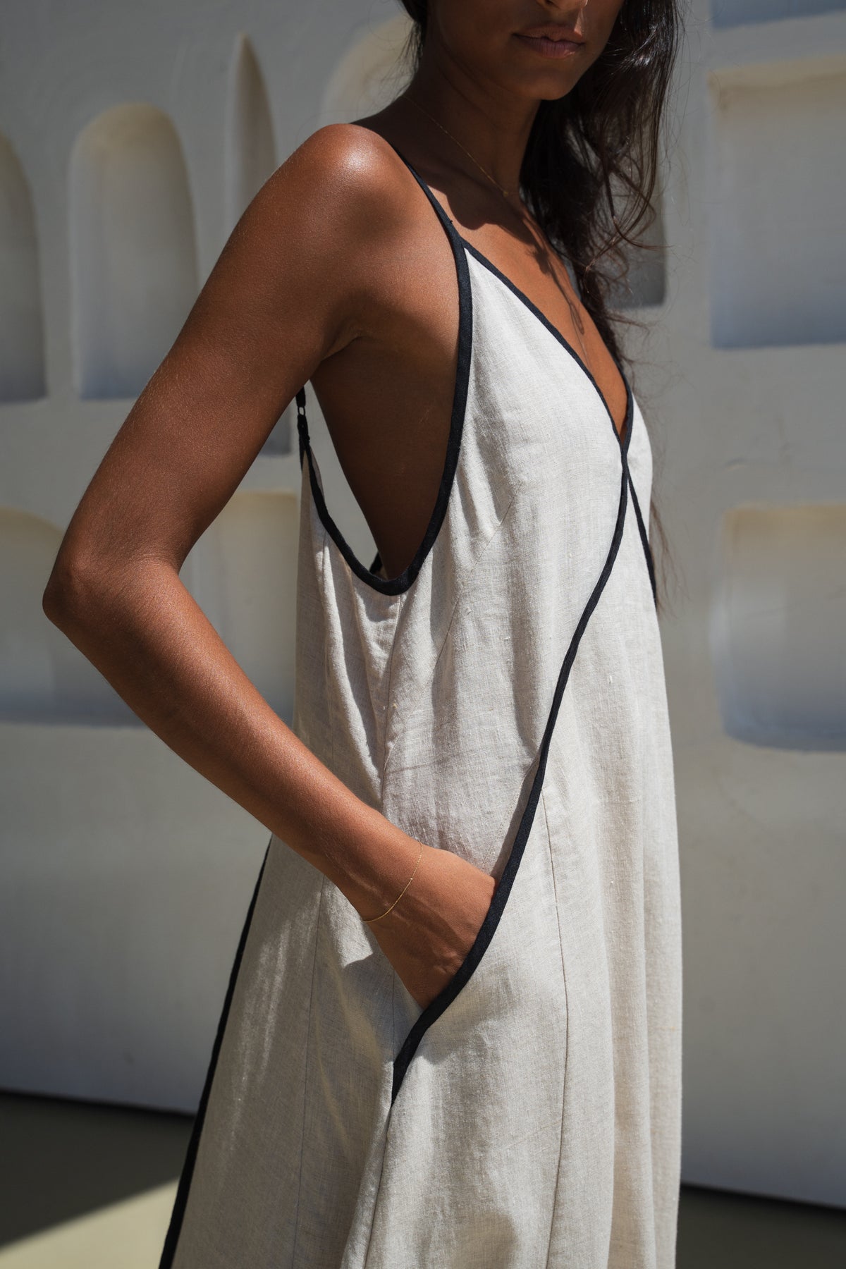 Close up back view of Lilly Pilly woman wearing an oatmeal Azalea dress with black straps and trim against a white wall.