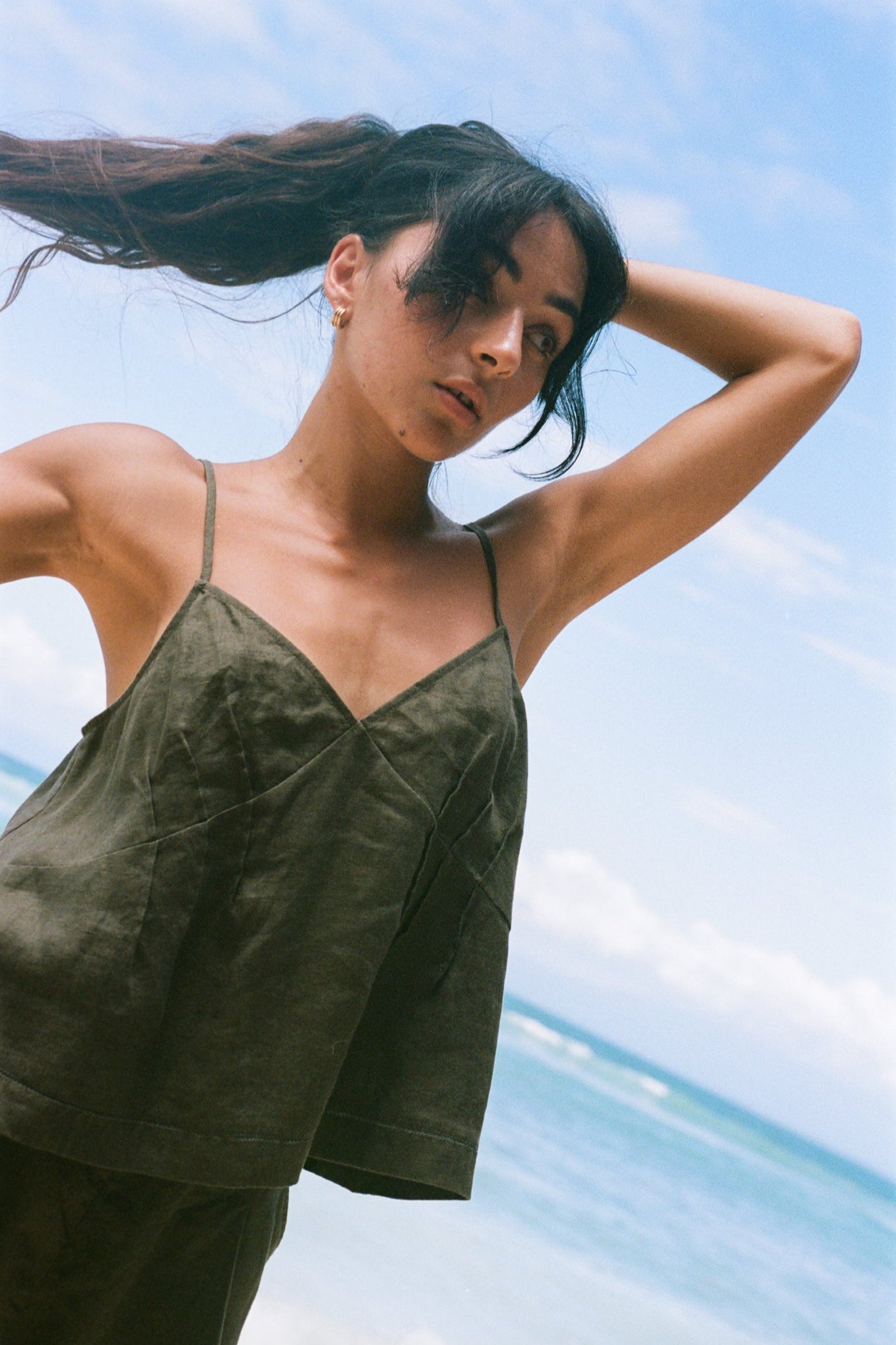 Close up view of LILLY PILLY woman wearing a khaki Bea linen cami top with a blurred blue sky background