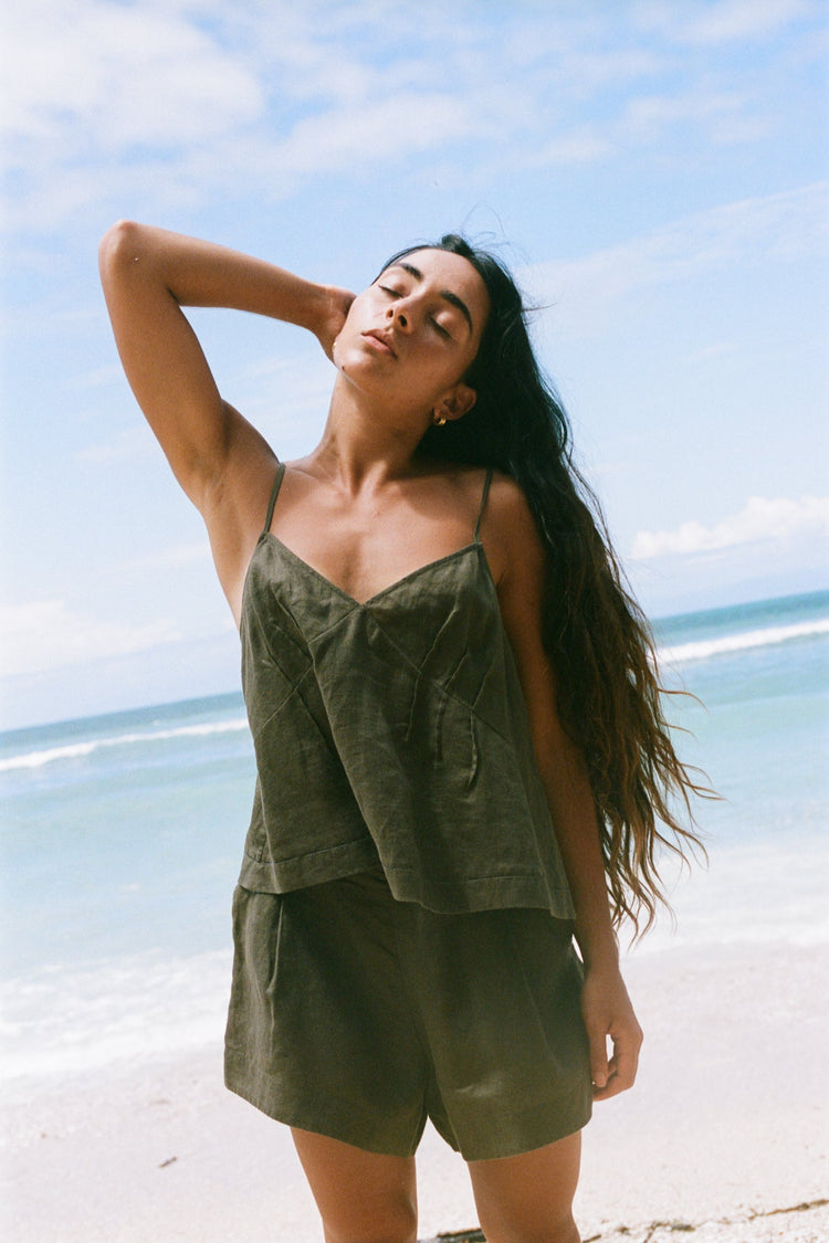 Bea Linen Cami in Khaki - full length, head tilted back, V-neckline and spaghetti straps, styled with matching Gaia Linen Shorts, beach and ocean backdrop - Lilly Pilly Collection