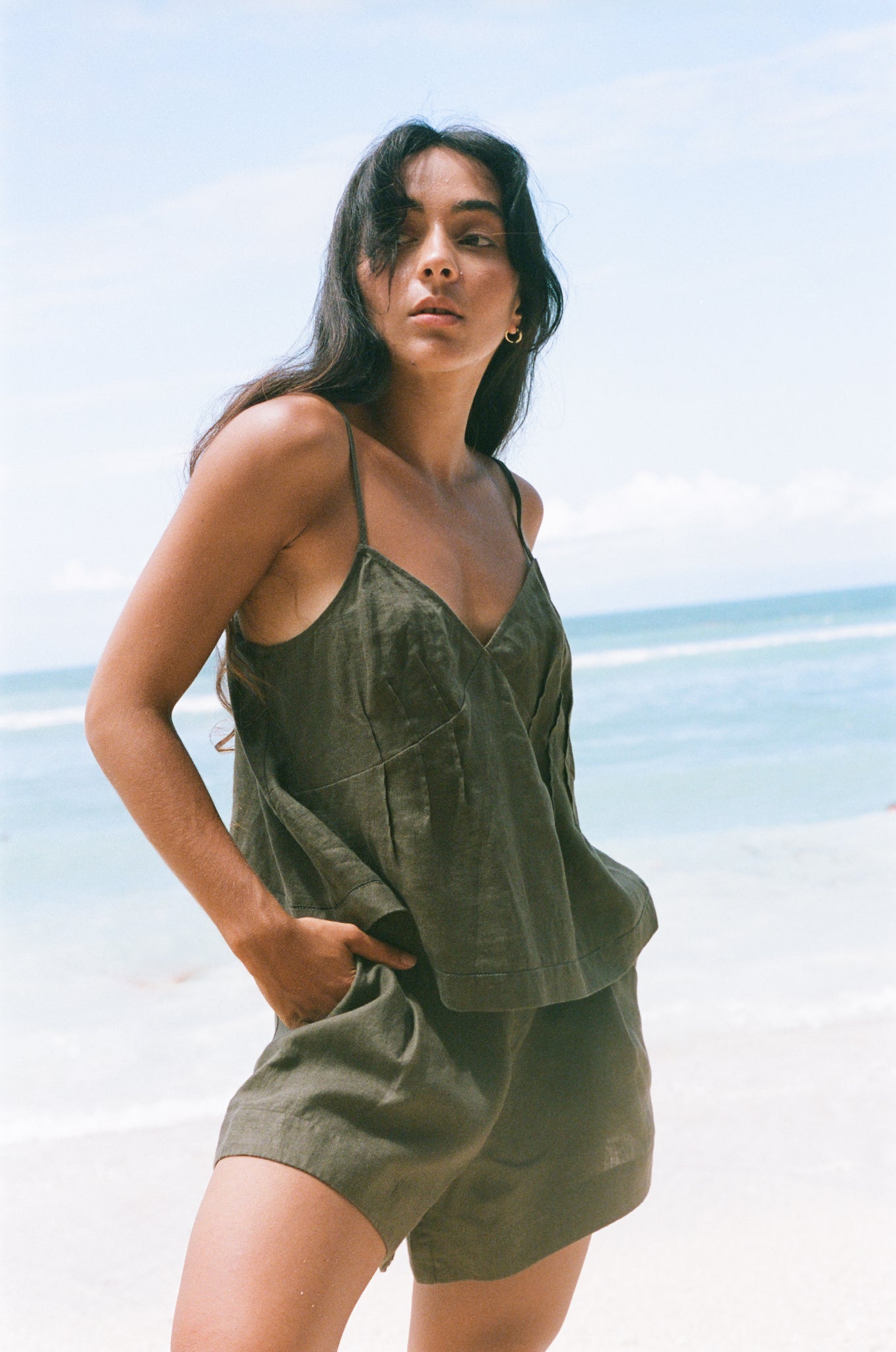Woman wearing a Bea and Gaia khaki linen outfit on a beach with clear blue sky.