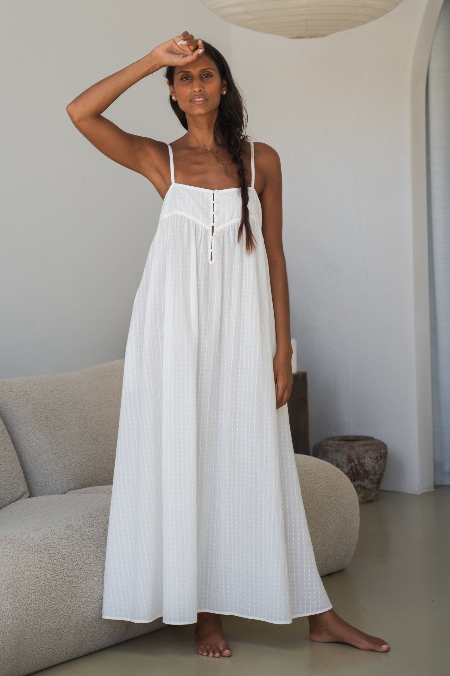 Woman wearing a white dress standing in a modern interior setting.