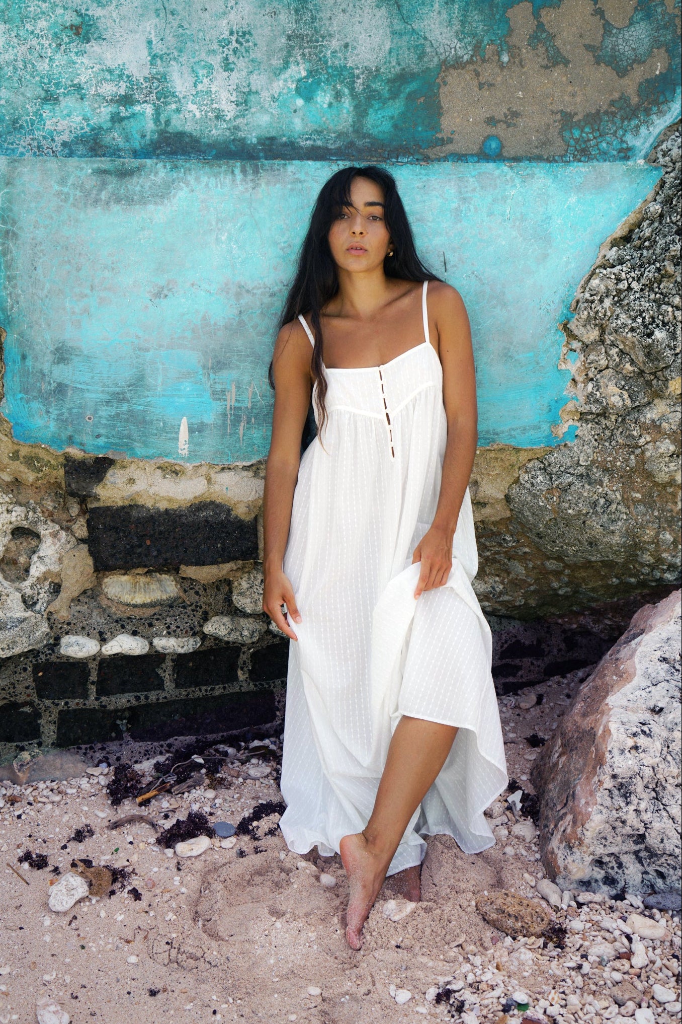 LILLY PILLY woman in a ivory Beatrice cotton dress standing against a textured blue wall.