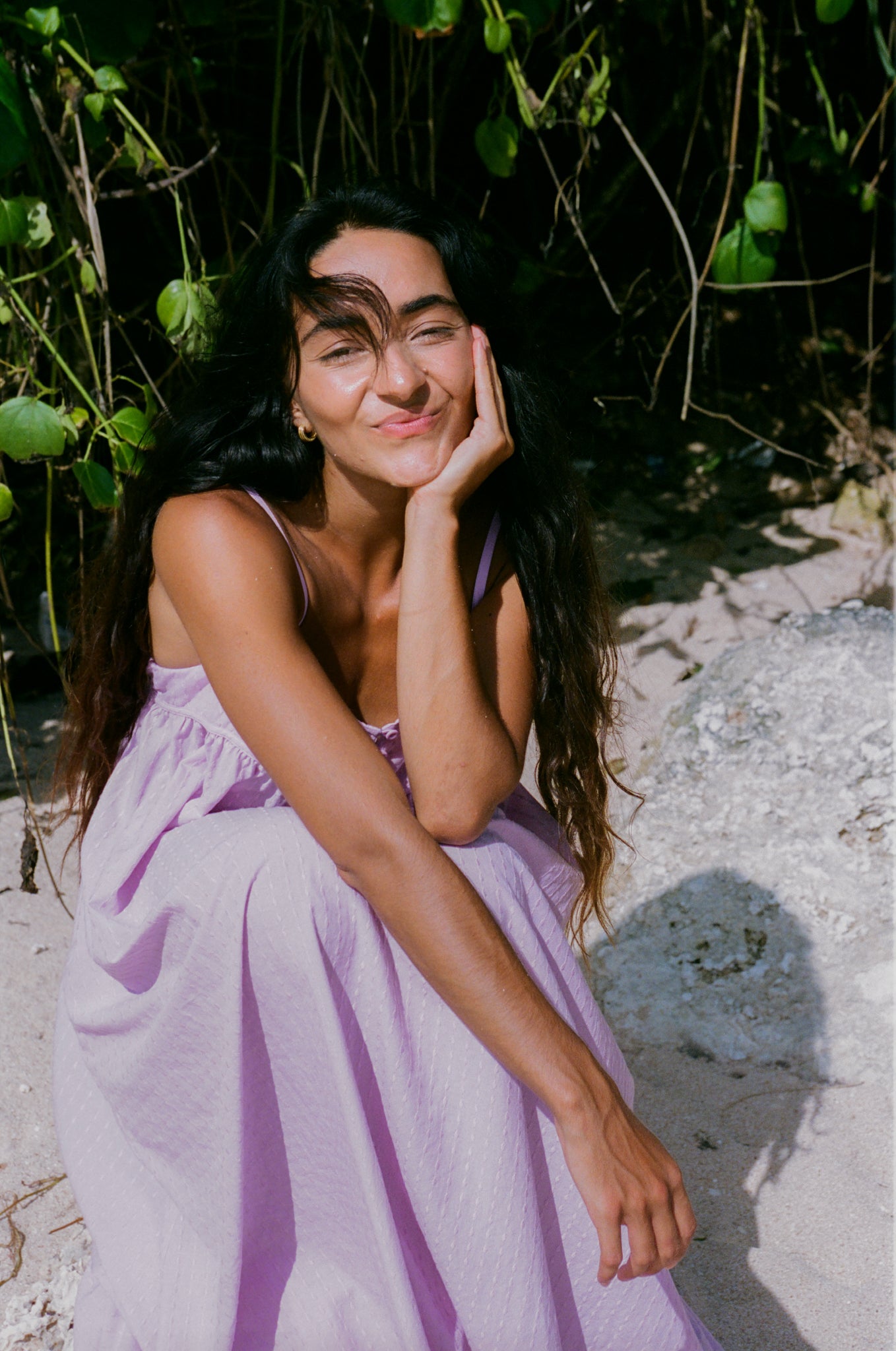 Woman in a purple dress sitting outdoors with greenery in the background