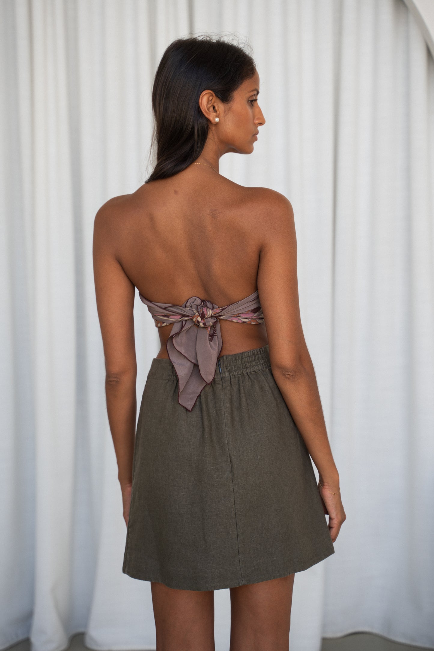 Woman wearing a strapless dress with a bow detail and khaki Betty linen skirt