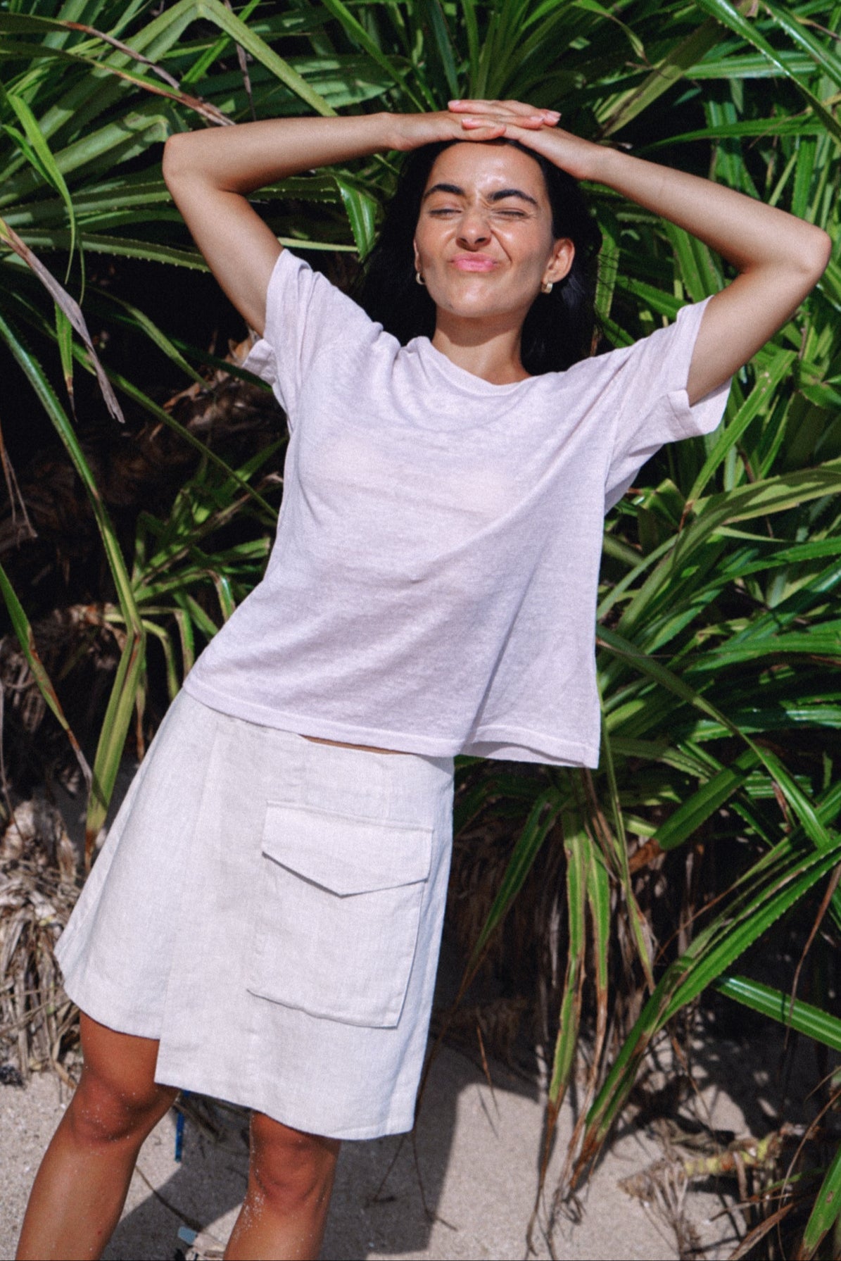 Woman in a light gray t-shirt and skirt standing outdoors with greenery in the background