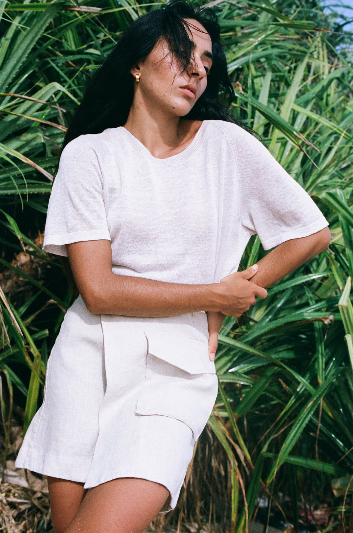 Woman in an oatmeal Betty linen skirt  standing in front of green foliage