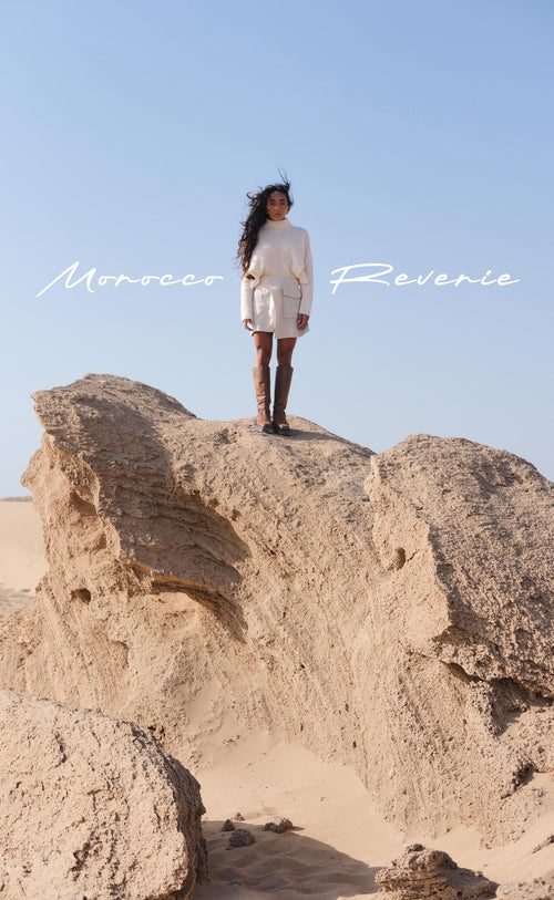 LILLY PILLY woman standing on a rocky outcrop in cashmere knit and linen skirt