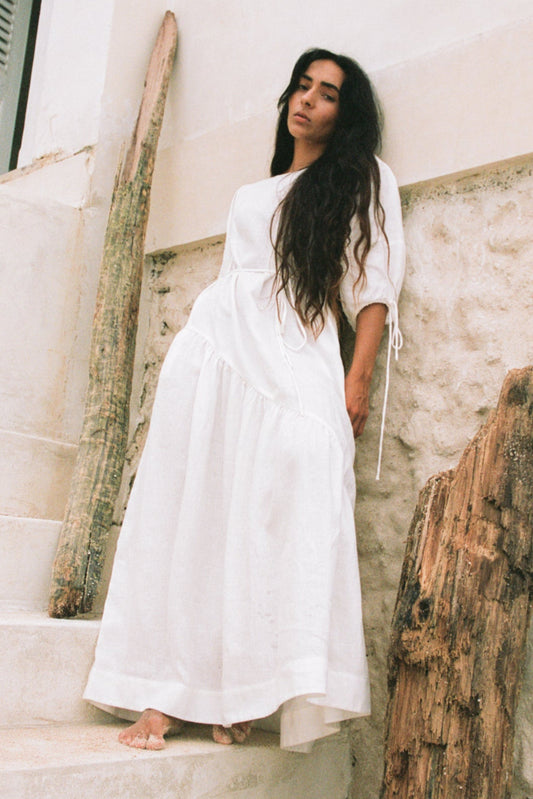 LILLY PILLY woman wearing Charlotte linen dress in Ivory standing by a white textured wall