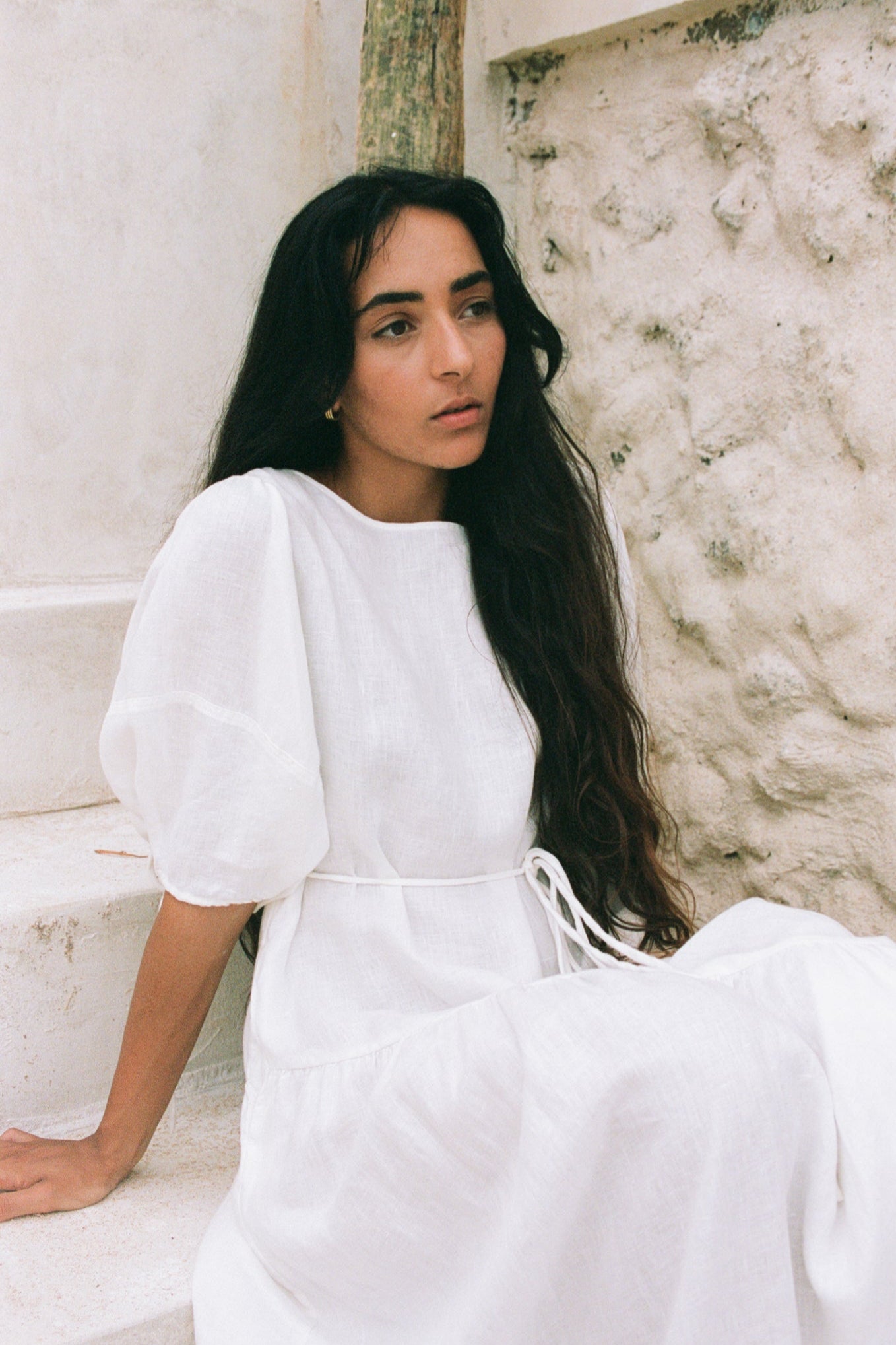 Woman in an ivory Charlotte linen dress sitting against a textured wall