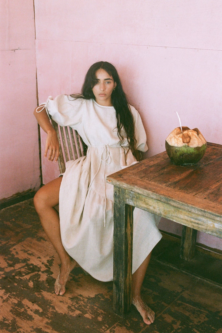 Charlotte Linen Maxi Dress in Oatmeal - front view sitting on a chair in a room with pink walls and a wooden table - Lilly Pilly Collection