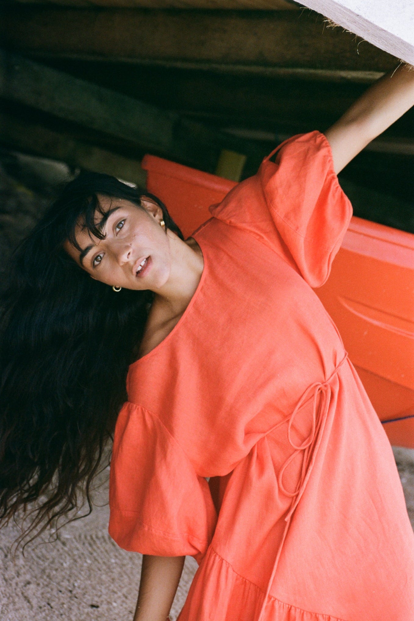 LILLY PILLY woman wearing a spritz coloured Charlotte dress on the sand under a wharf with a boat in the background