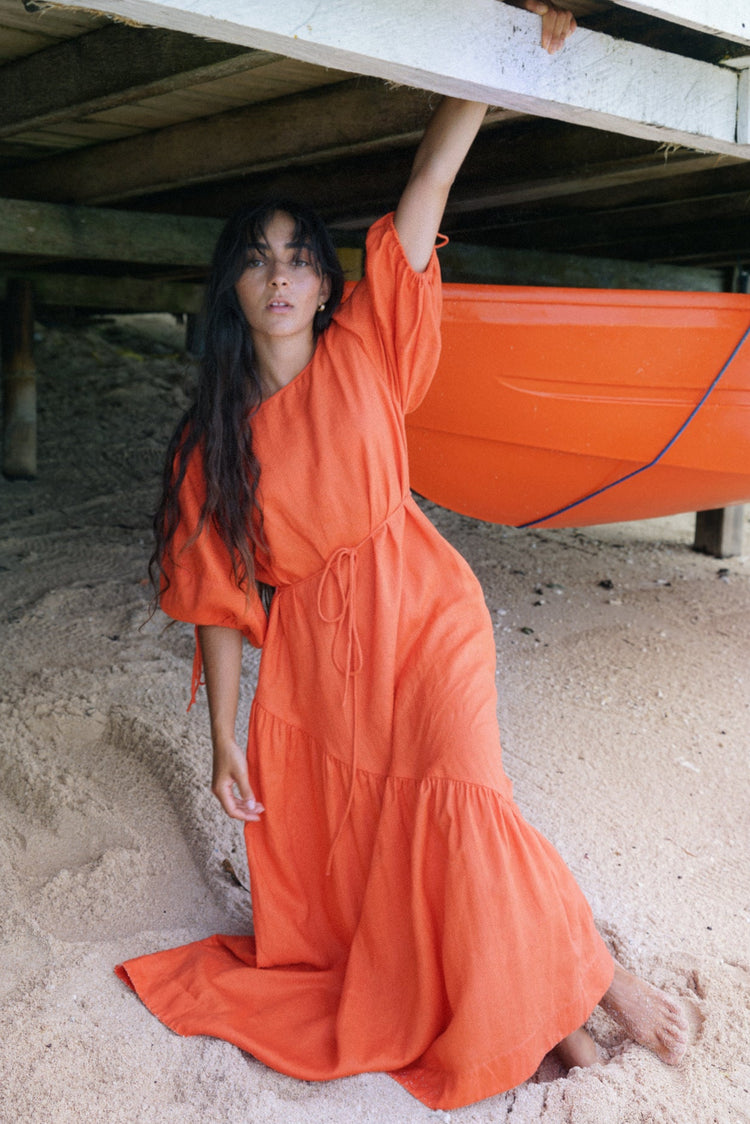 Charlotte Linen Maxi Dress in Spritz Orange - standing under a wooden boathouse - Lilly Pilly Collection