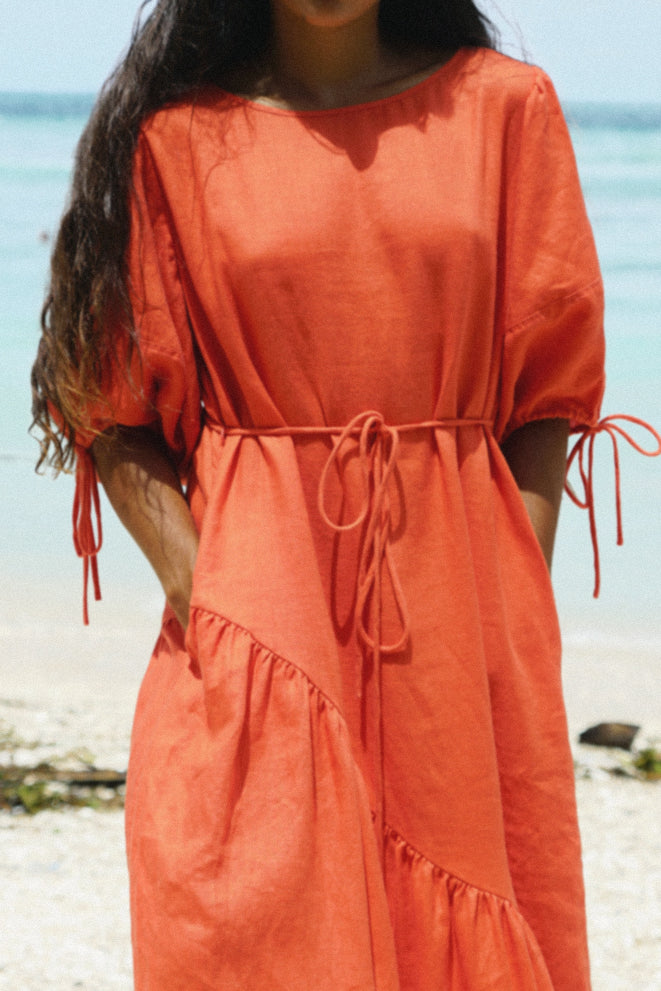 LILLY PILLY woman wearing a spritz coloured Charlotte linen dress on the sand by the waters edge