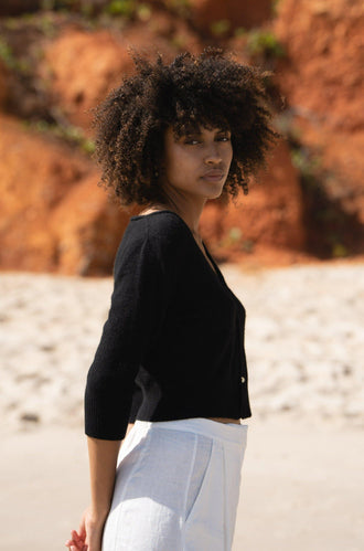 Jade Cashmere Cardigan in Black - side view, worn with wide-leg trousers, standing on red rock beach - Lilly Pilly Collection