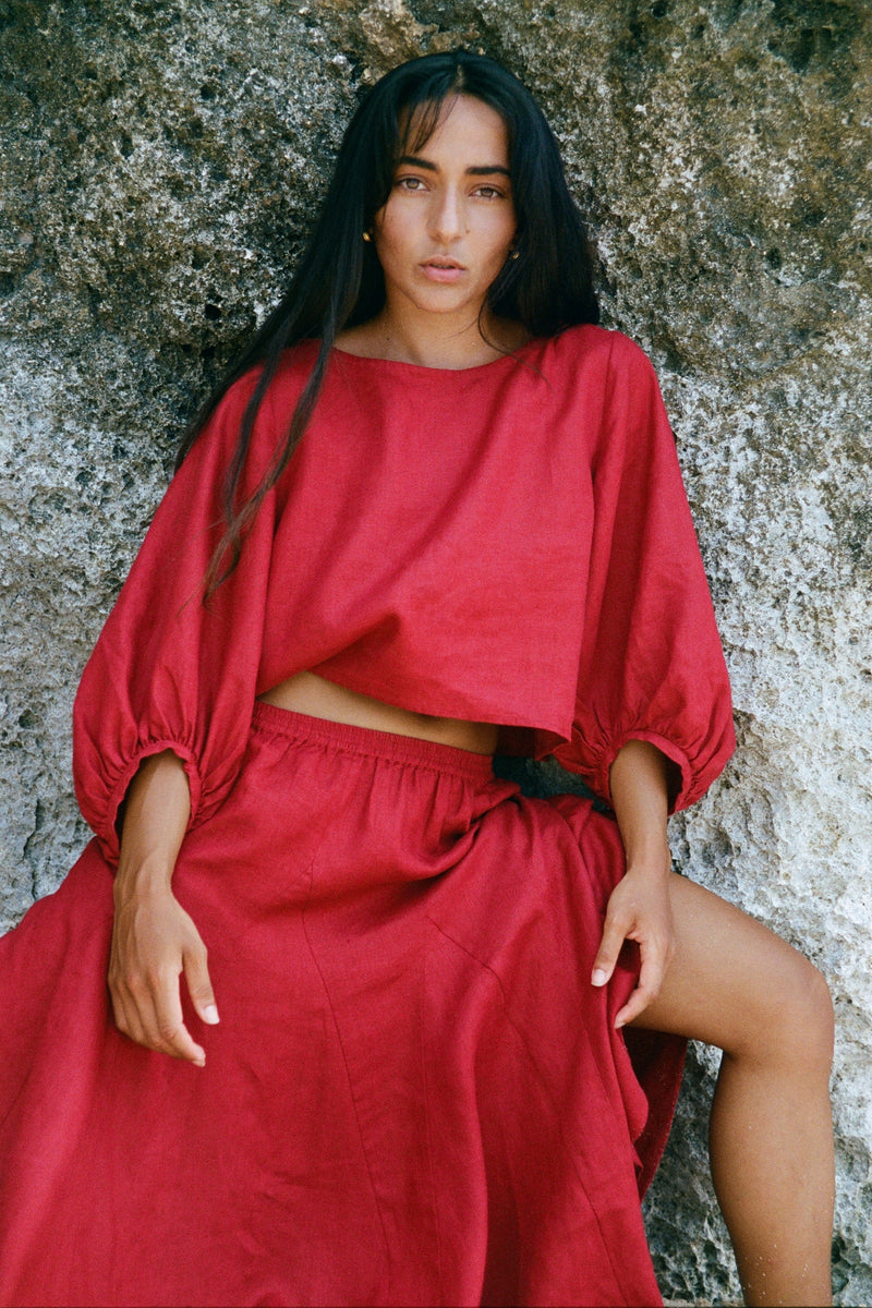 Demi Linen Top in Cherry Red - woman seated against rocks, round neckline and puff sleeves, styled with matching Riley Linen midi skirt - Lilly Pilly Collection
