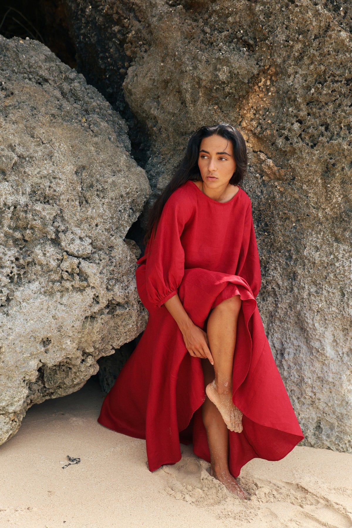 Demi Linen Top in Cherry Red - full length, woman seated on sand against rocks, puff sleeves and cropped hem, styled with matching Riley Linen Skirt - Lilly Pilly Collection