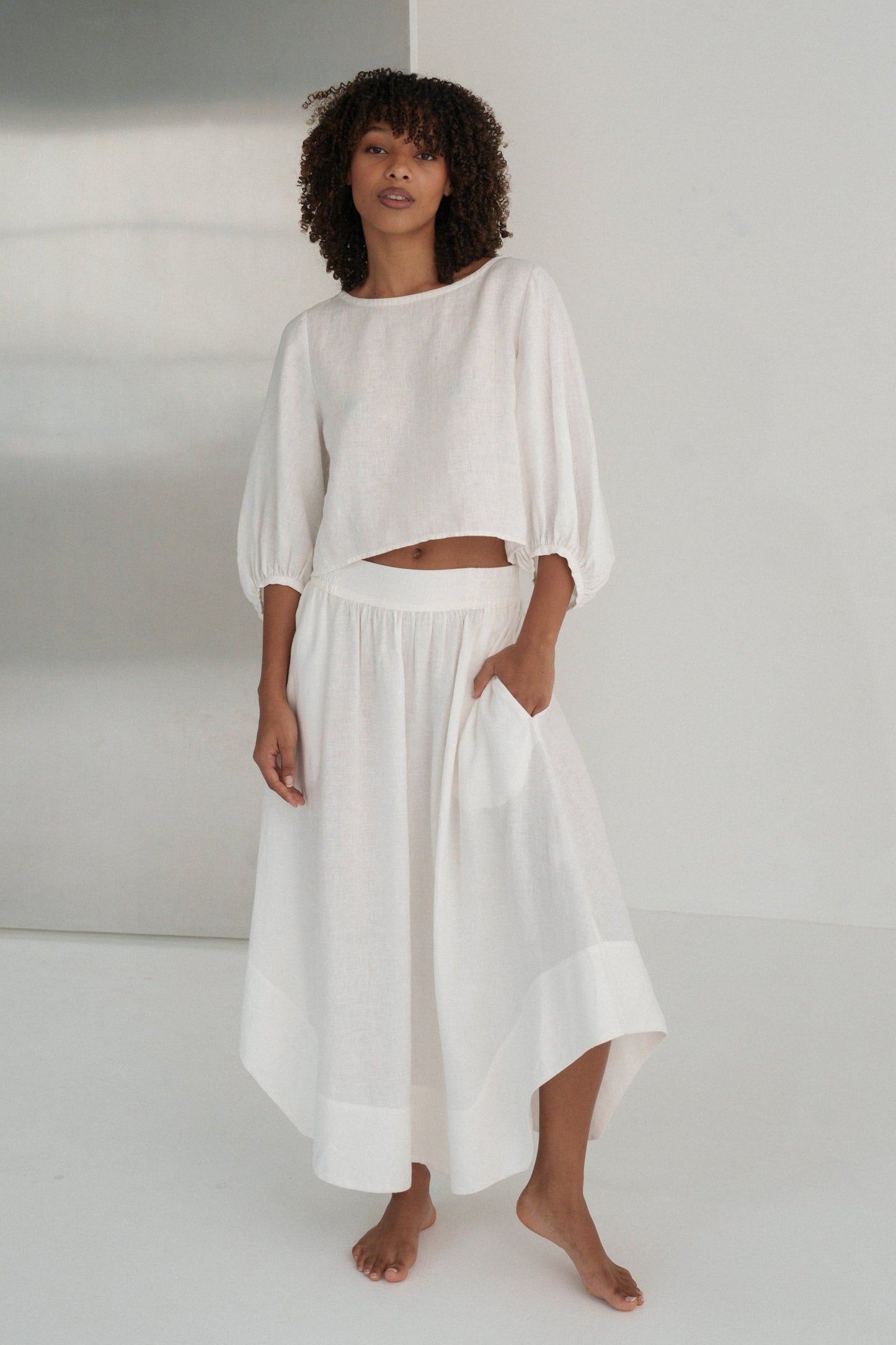 LILLY PILLY woman wearing an ivory Demi linen top and Hannah skirt standing against a plain background