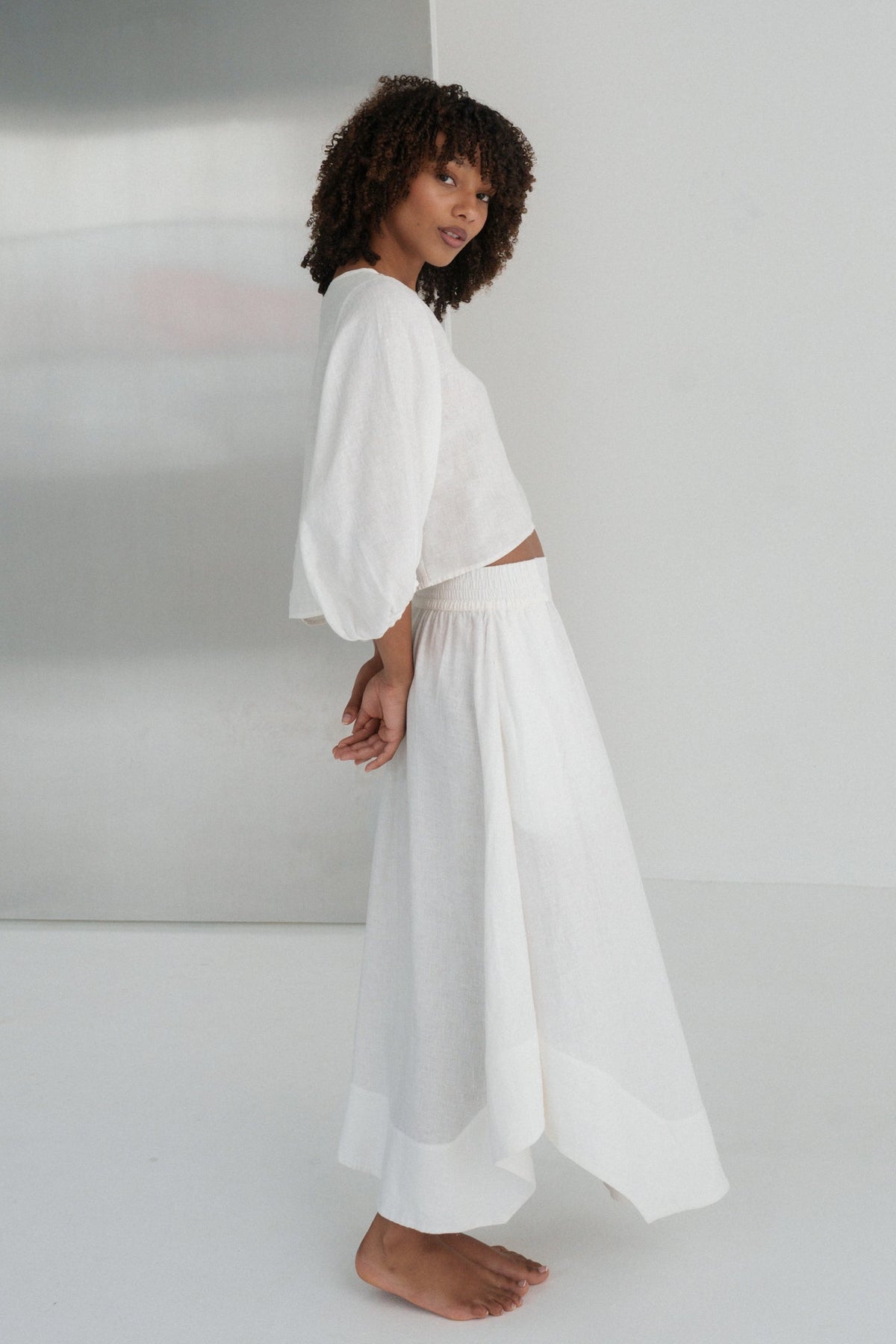 LILLY PILLY woman wearing an ivory Demi linen top and Hannah skirt outfit standing against a plain white wall
