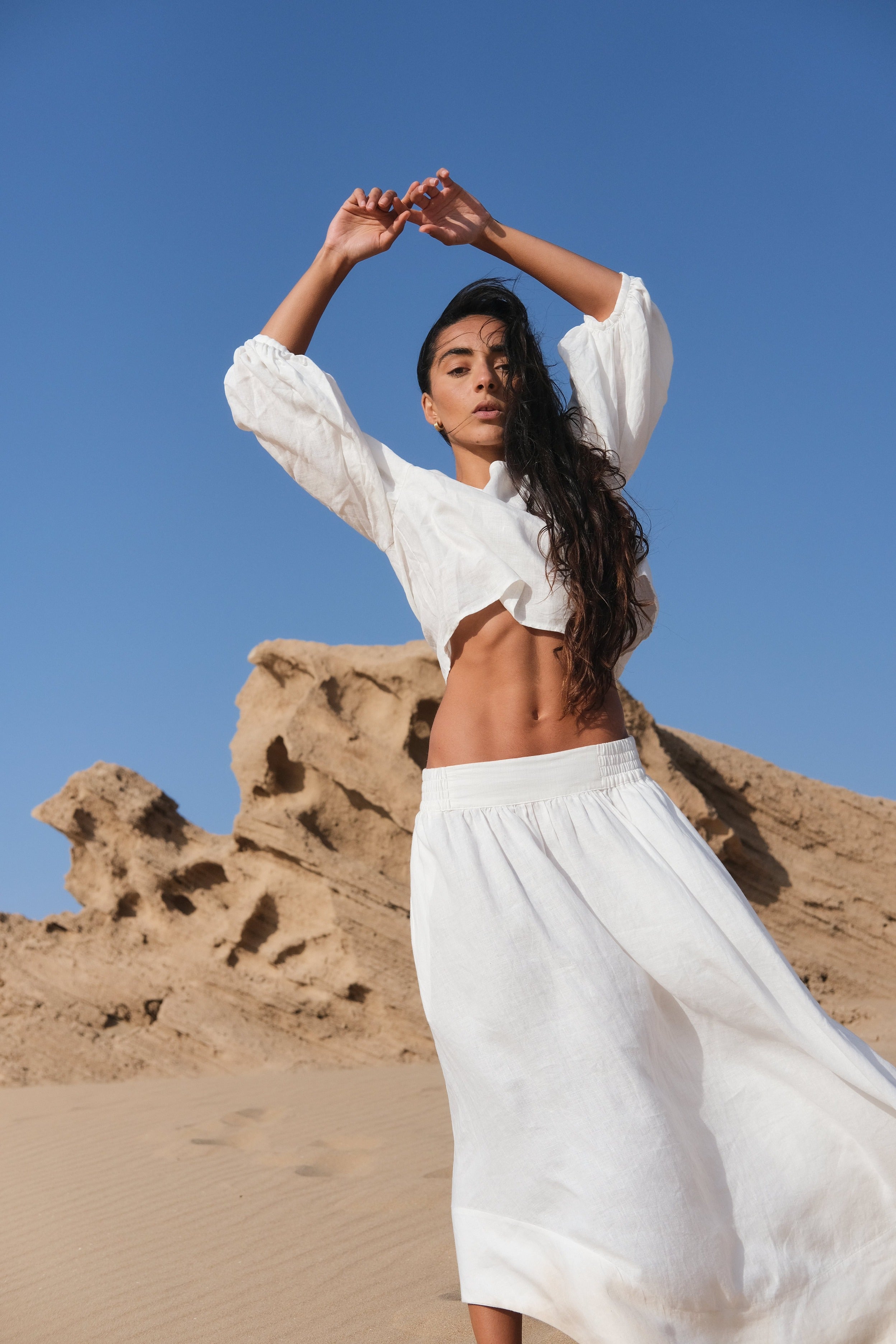 LILLY PILLY woman wearing an ivory Demi linen top and Hannah skirt outfit standing in a desert landscape with clear blue sky