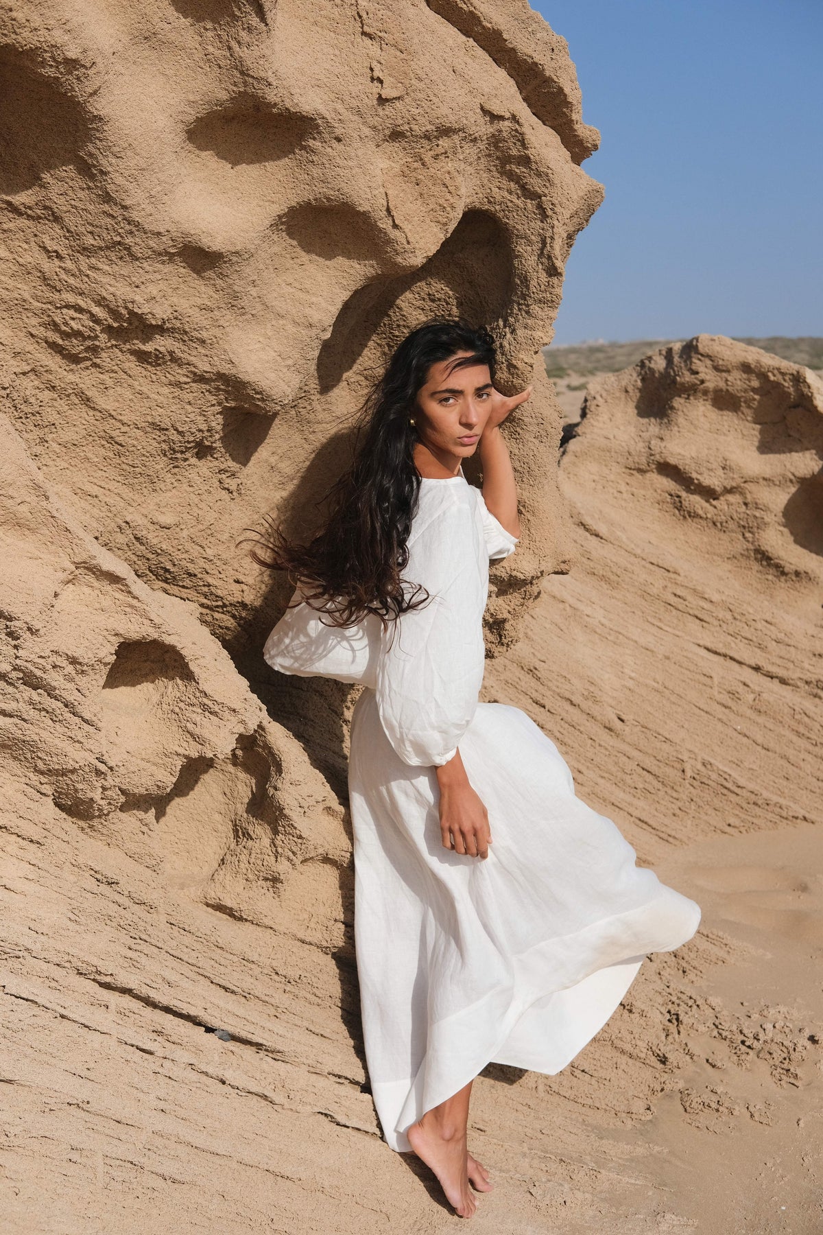 LILLY PILLY woman wearing an ivory Demi linen top and Hannah skirt standing against a rocky desert background