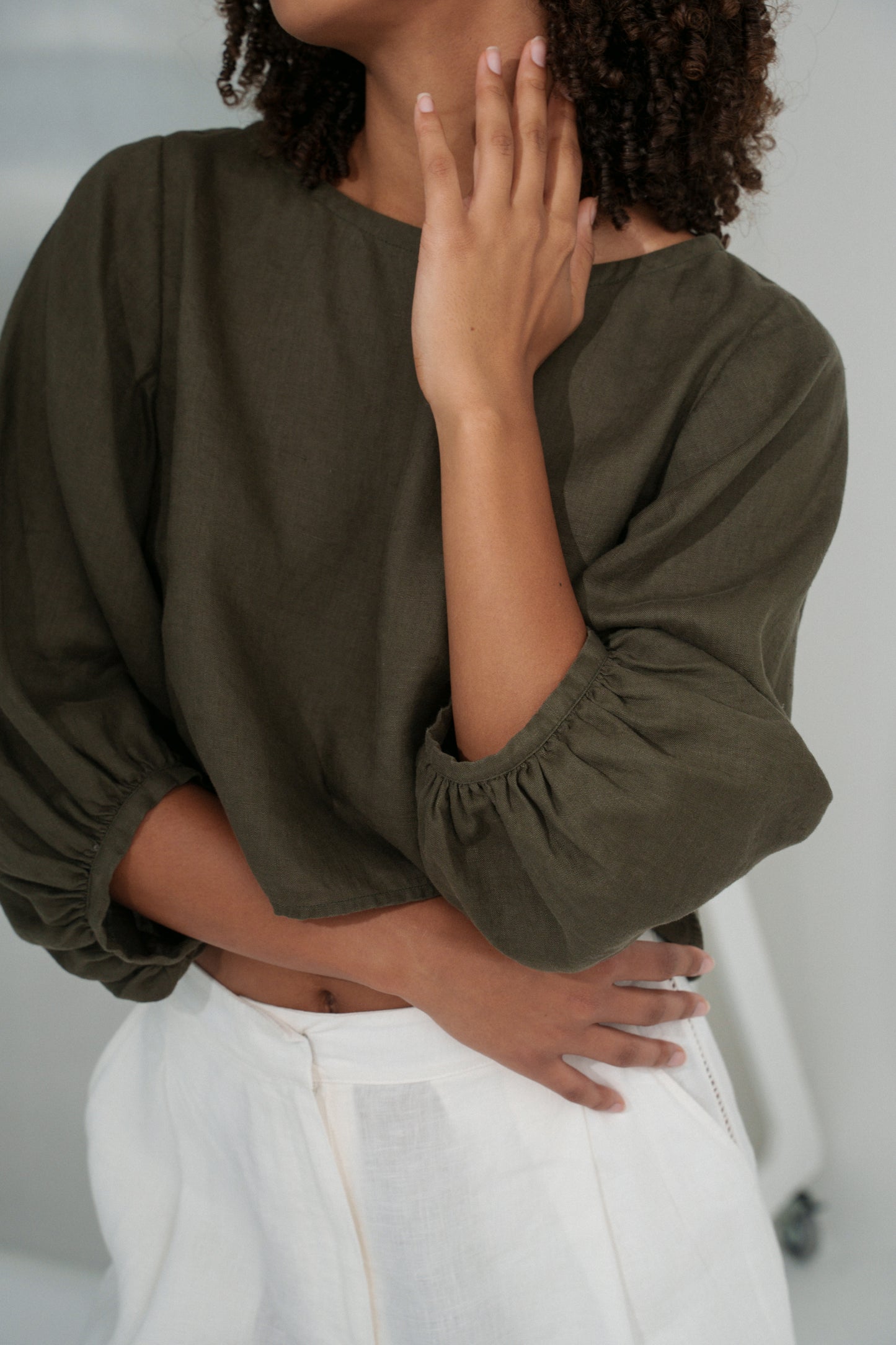 Close up of LILLY PILLY woman wearing a khaki green Demi linen top and ivory Ivy linen pants against a plain background