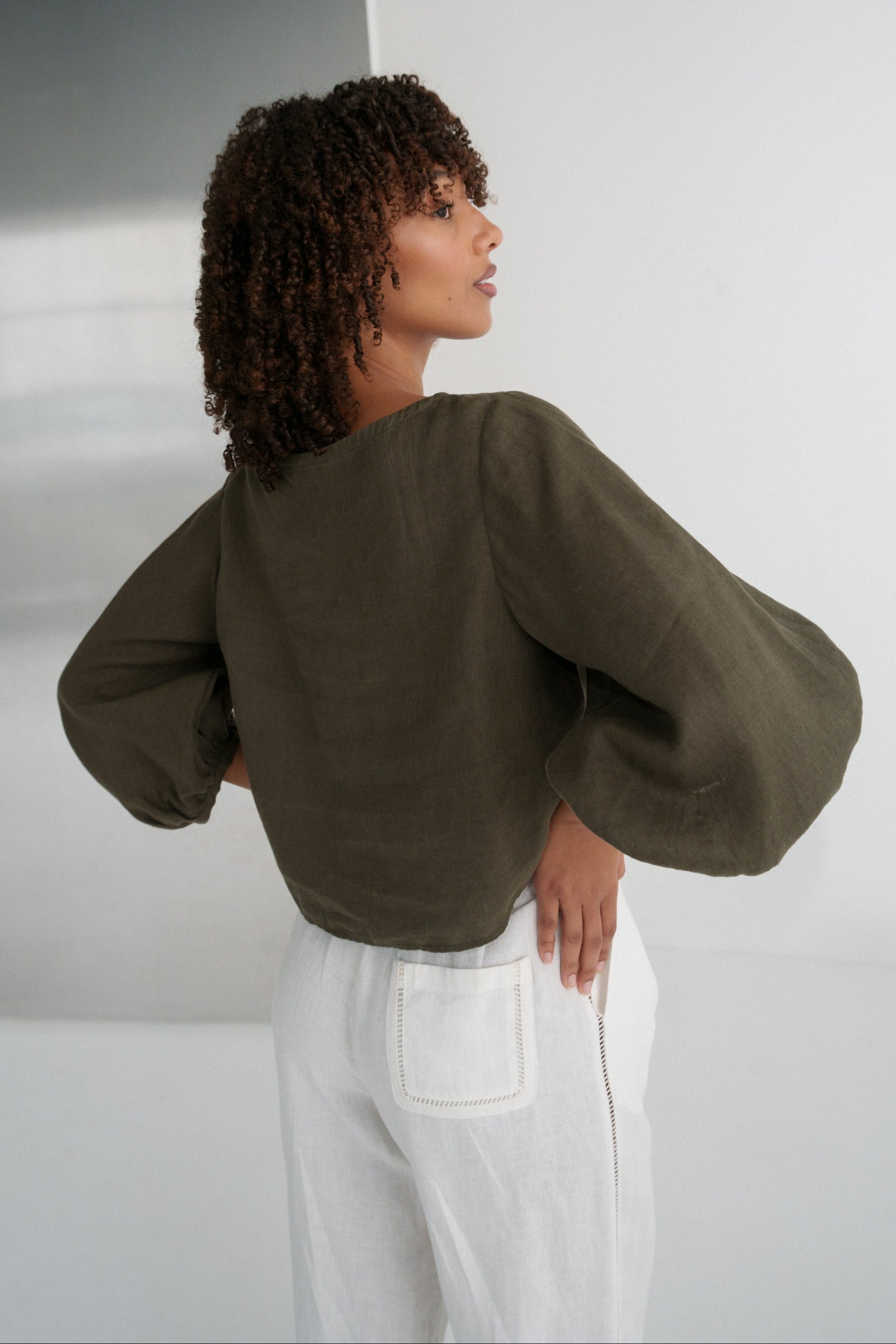 LILLY PILLY woman wearing a khaki green Demi linen top and ivory Oli linen pants against a plain background showing back view