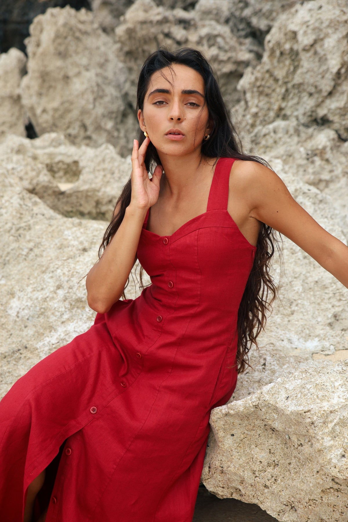 Eden Linen Midi Dress in Cherry Red - woman seated on rocks, close-up of sweetheart neckline and button-front detail - Lilly Pilly Collection