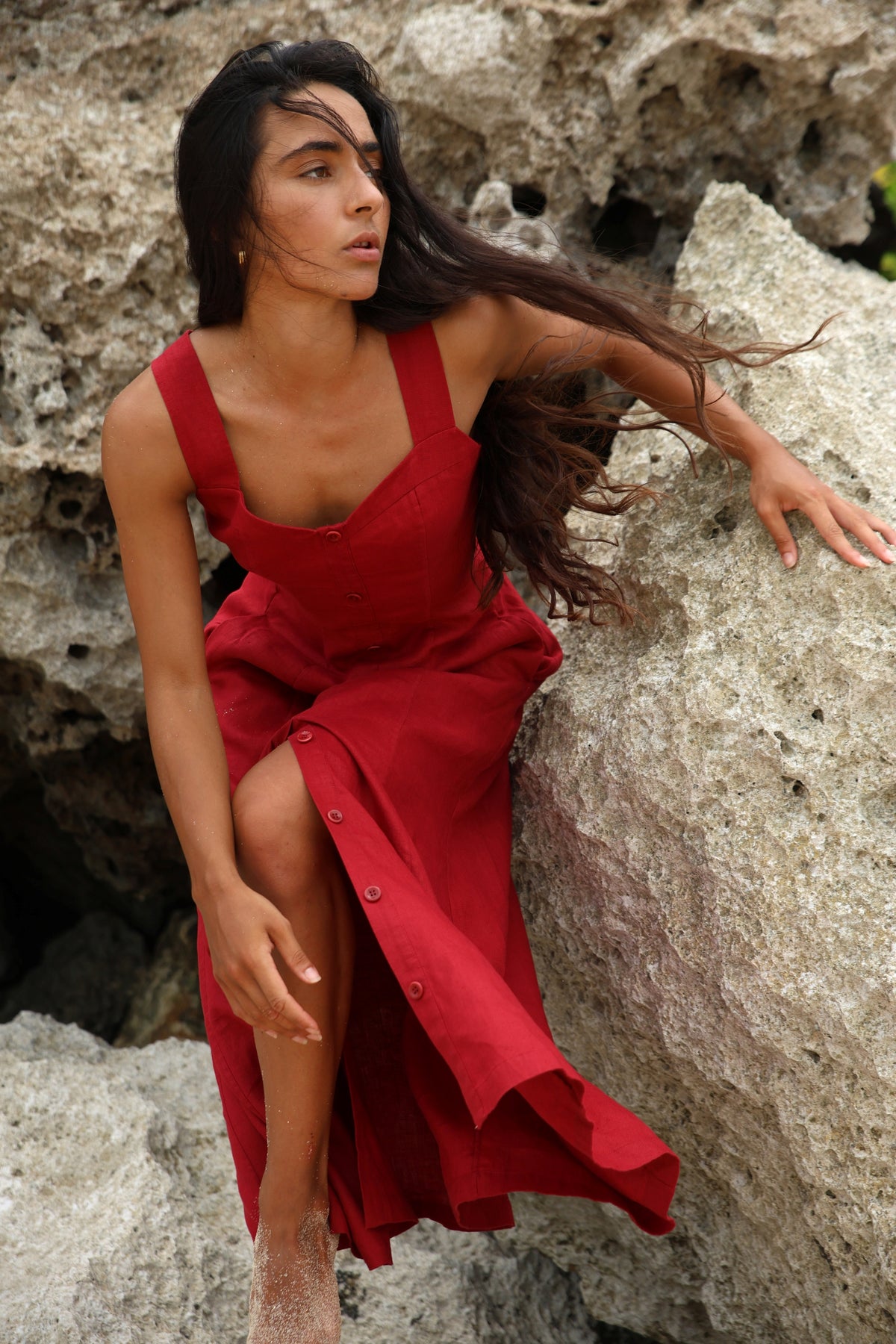 Eden Linen Midi Dress in Cherry Red - woman seated on rocks, sweetheart neckline and button-front placket, coastal backdrop - Lilly Pilly Collection