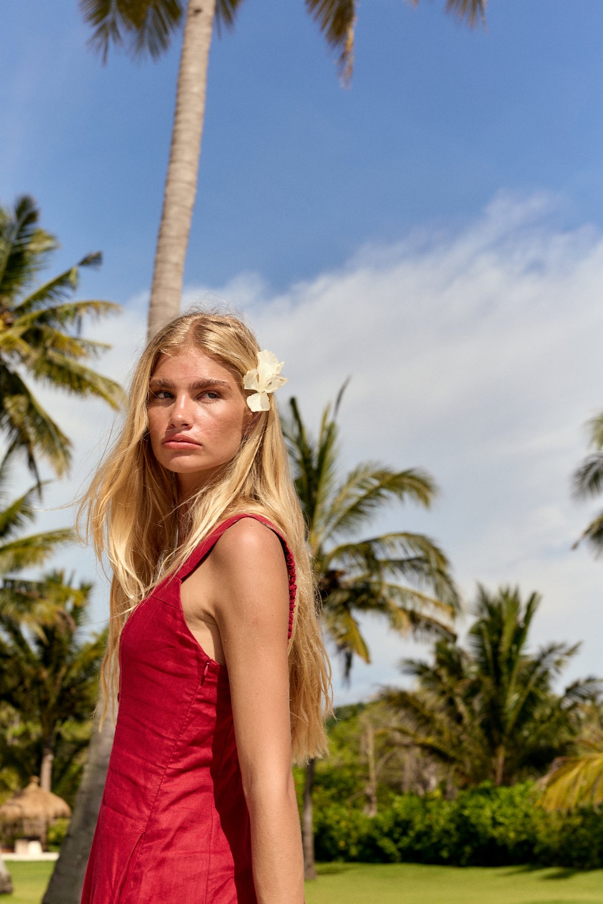 Eden Linen Midi Dress in Cherry Red - woman looking over shoulder, sweetheart neckline and wide straps, tropical backdrop - Lilly Pilly Collection