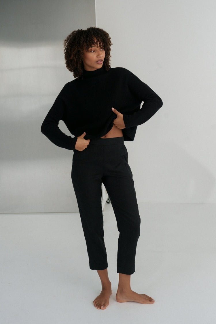 Emer Linen Pants in Black - full length front view, woman wearing Black tapered linen pants with black cropped turtleneck knit, studio backdrop - Lilly Pilly Collection