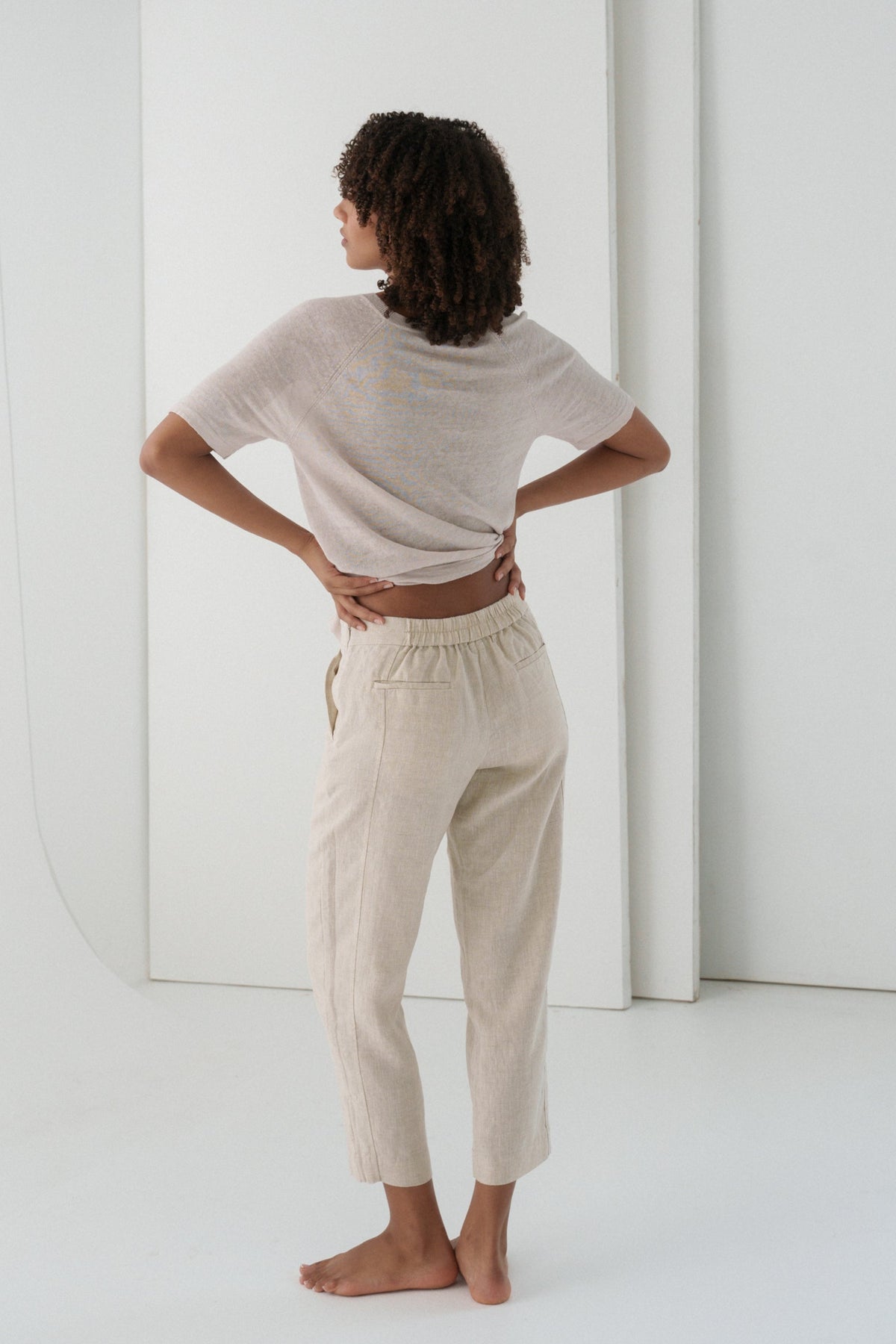 LILLY PILLY woman wearing a oatmeal Emer linen pants standing in a minimalistic room.