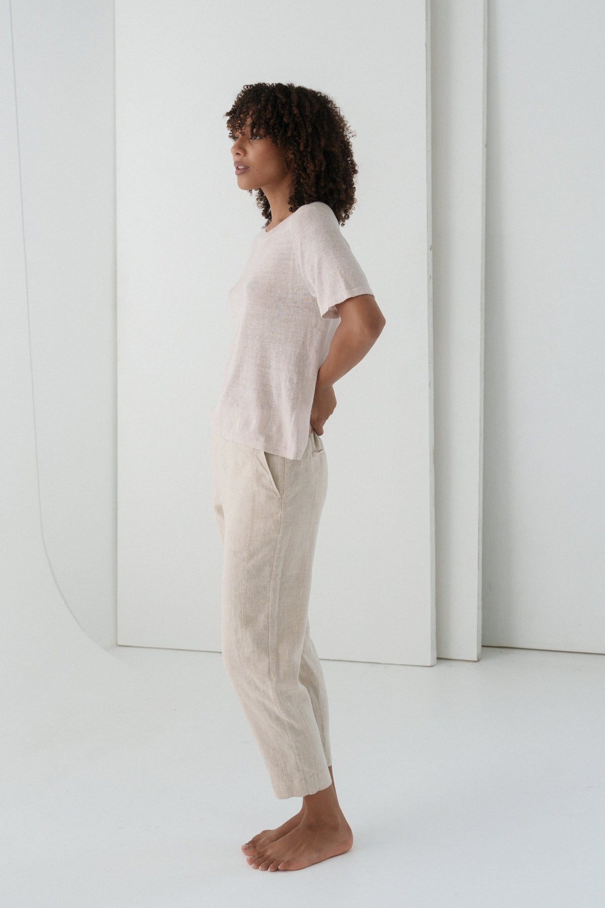 LILLY PILLY woman wearing a oatmeal Emer linen pants standing in a minimalistic room with white walls and floor.