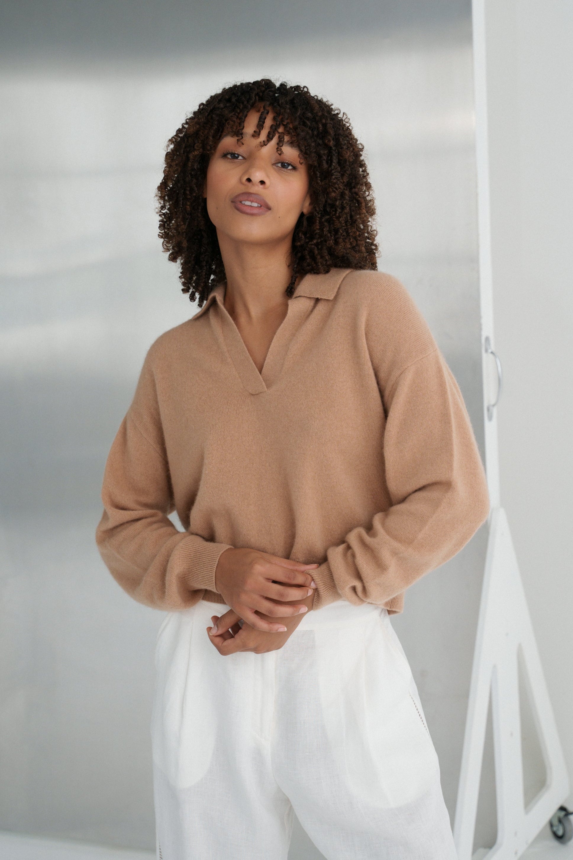 LILLY PILLY woman wearing a camel coloured Emma cashmere merino knit sweater and ivory white Ivy pants against a neutral background