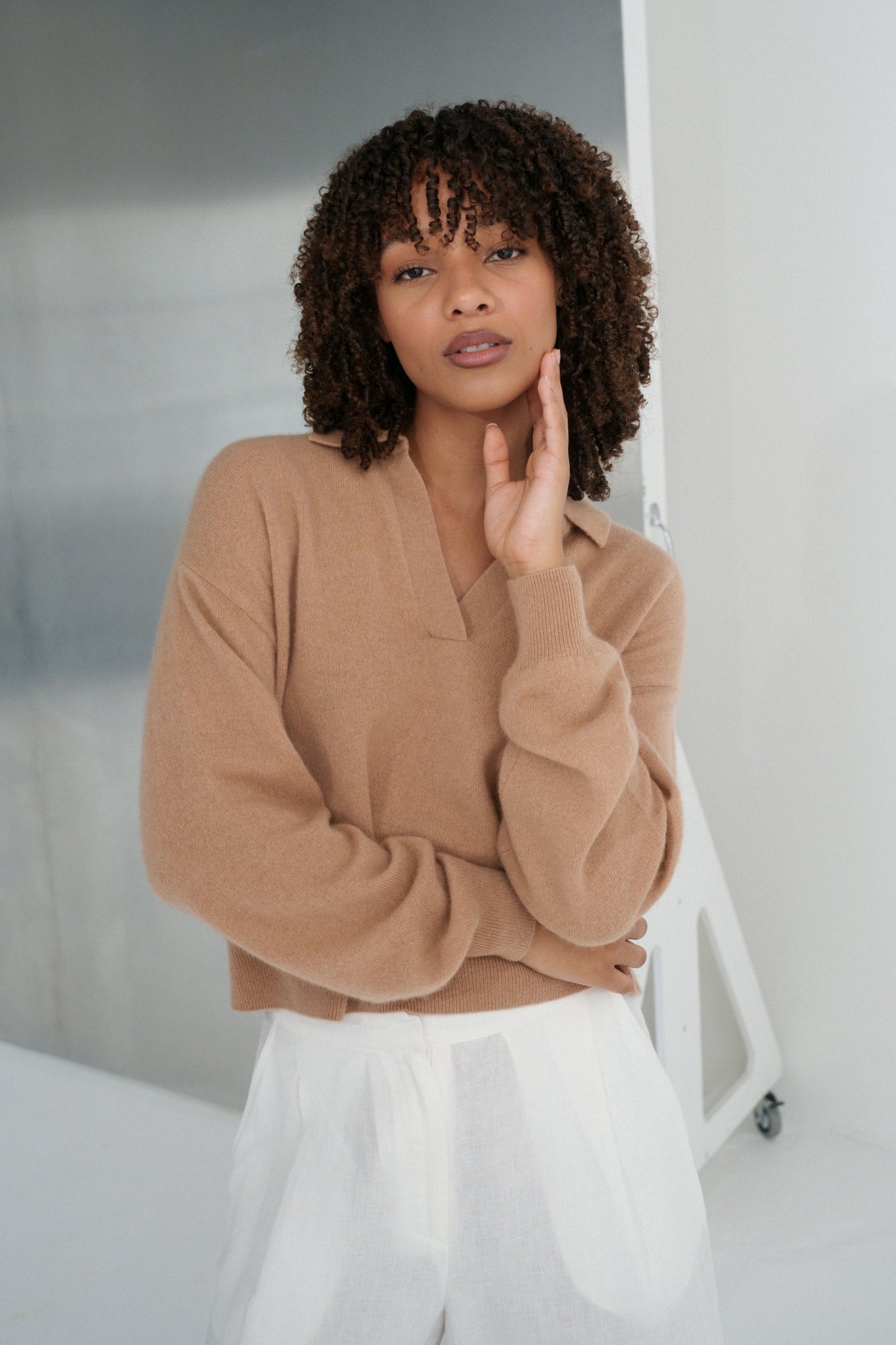 LILLY PILLY woman wearing a camel coloured Emma cashmere merino knit sweater and white Oli pants against a neutral background