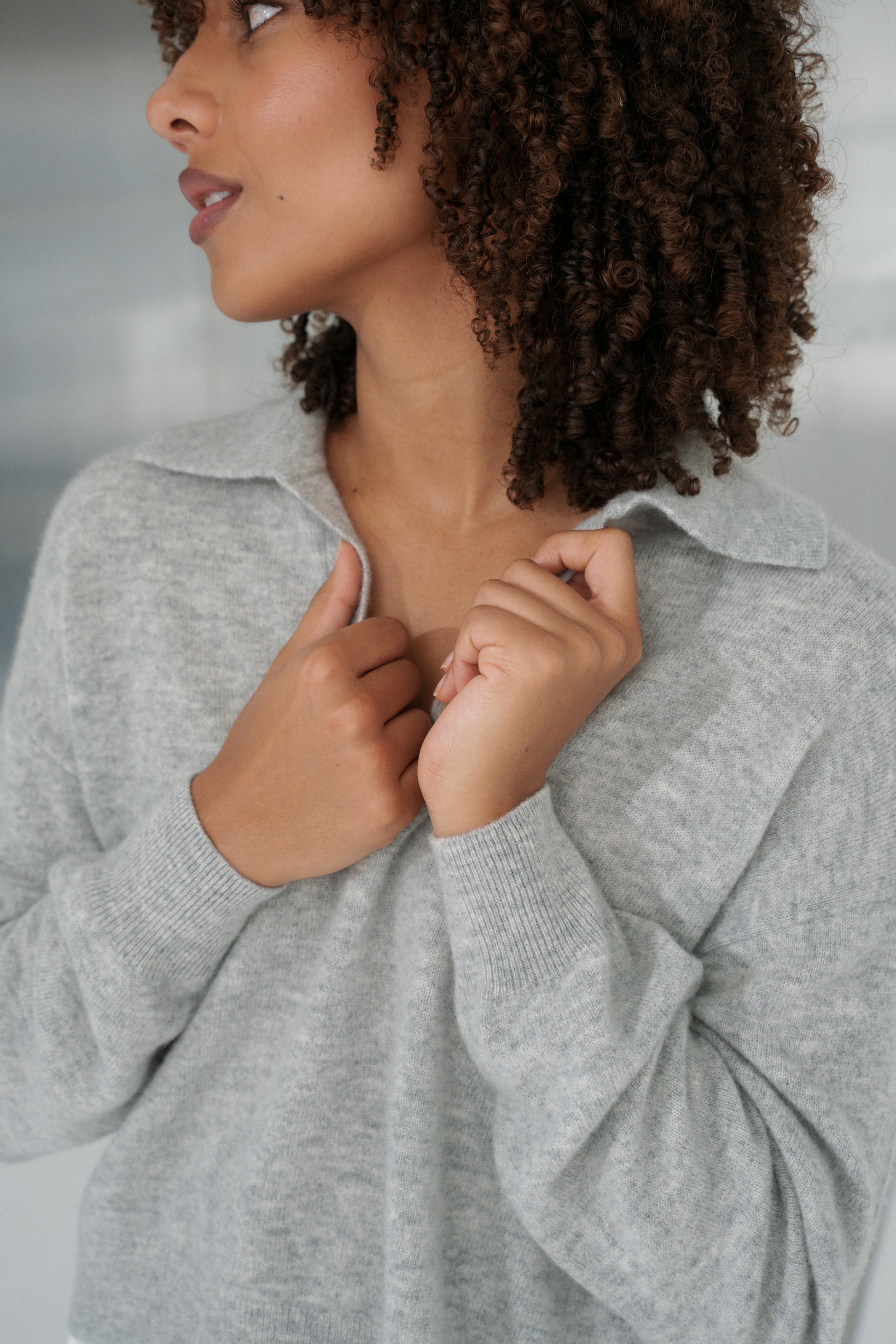 Close up of LILLY PILLY woman holding the collar of her grey marle coloured Emma cashmere merino knit sweater and ivory white pants with a blurred background