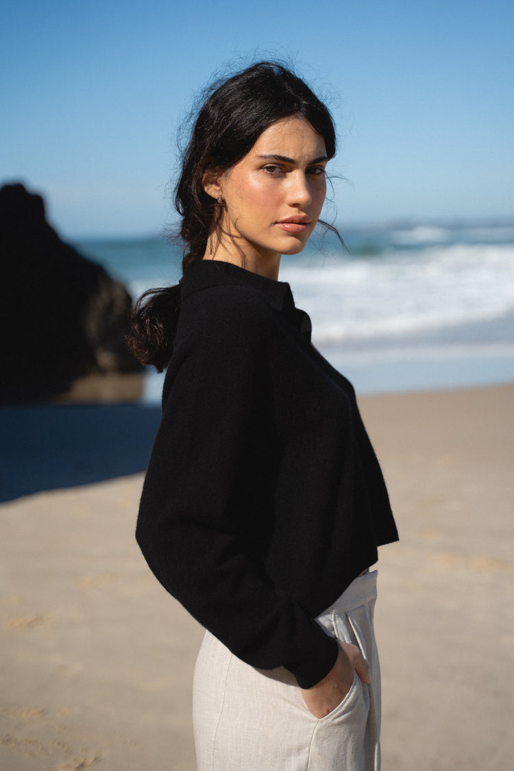 Emma Cashmere Knit in Black - side profile, collared knit, standing on beach with ocean backdrop - Lilly Pilly Collection