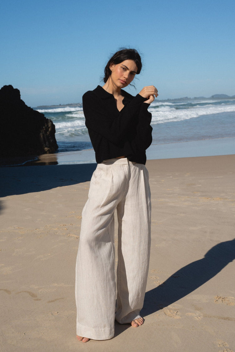 Emma Cashmere Knit in Black - full length front view, worn with wide-leg trousers, standing on beach with ocean and rocks backdrop - Lilly Pilly Collection