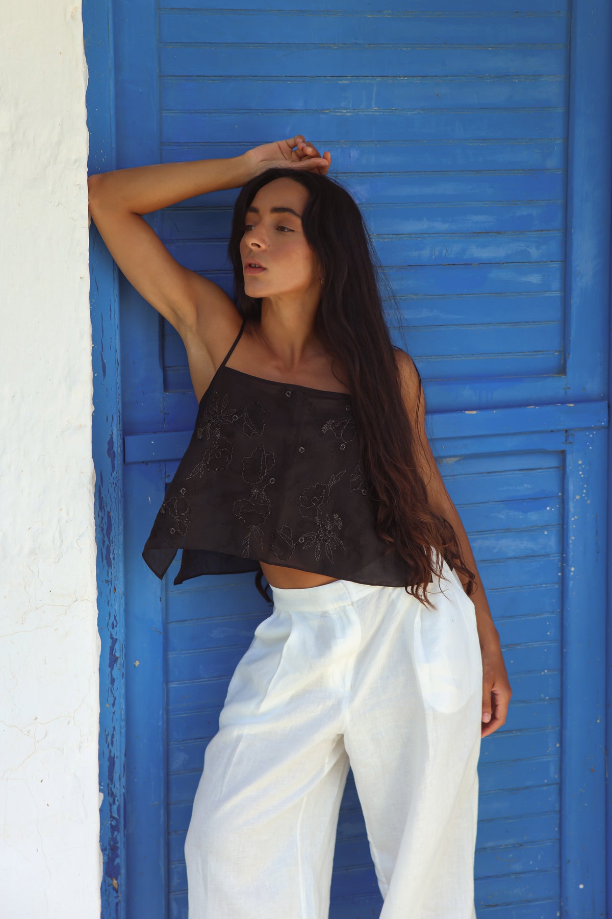 Flora Ramie Cami in Black - full length, floral embroidery and thin straps, worn with Oli Pants in Ivory, hand in hair, blue shutters backdrop - Lilly Pilly Collection