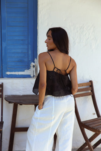 Flora Ramie Cami in Black - back view, tie-back detail and floral embroidery, worn with Oli Pants in Ivory, blue shutters backdrop - Lilly Pilly Collection