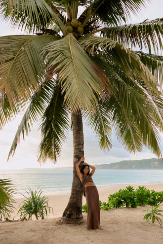 Frankie Silk Cami in Chocolate - full length, arm raised against palm tree, styled with matching linen maxi skirt, tropical beach - Lilly Pilly Collection