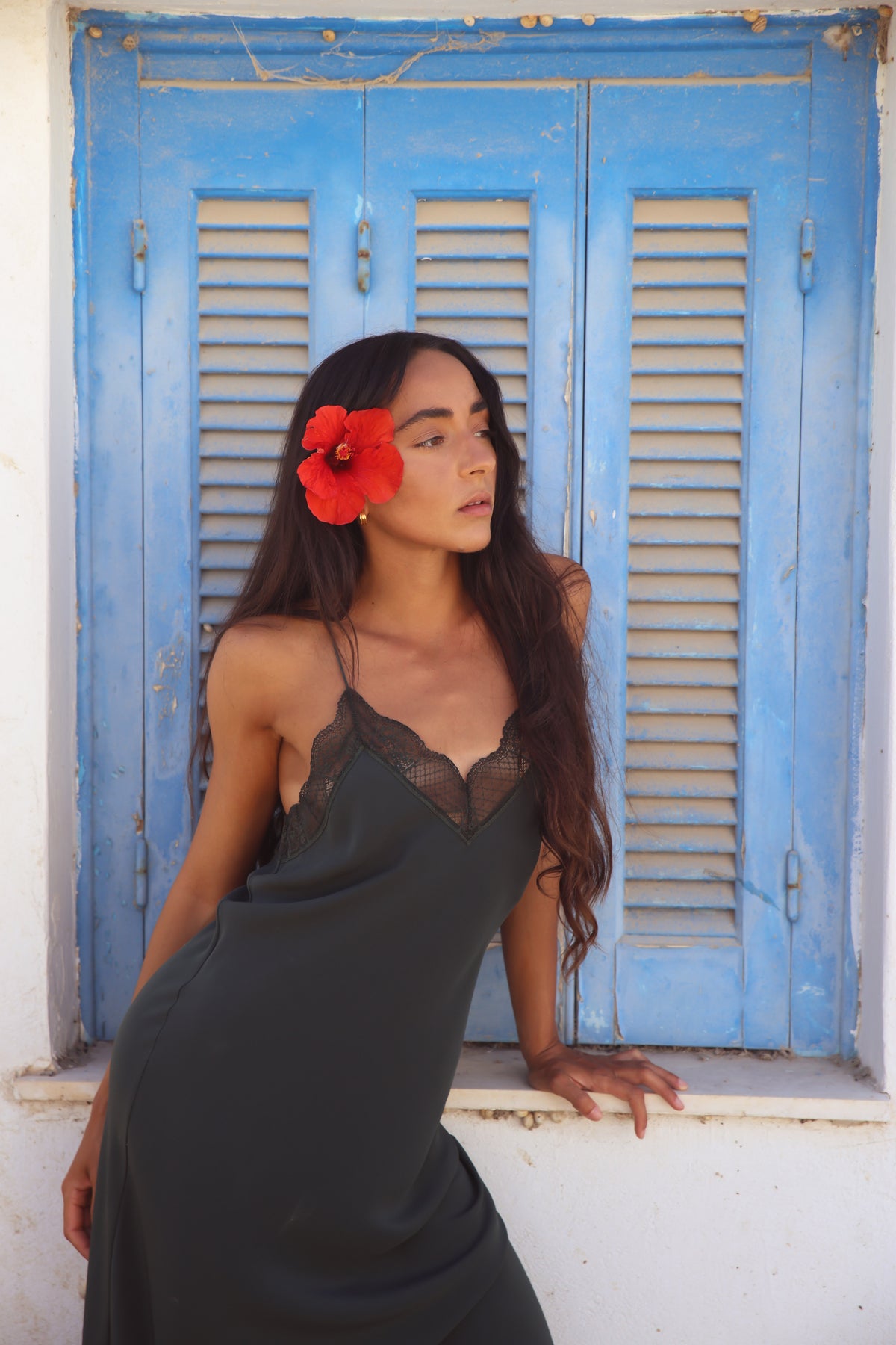 Freya Silk Midi Slip Dress in Forest Green - three-quarter view with lace neckline detail, model looking away against blue shutters - Lilly Pilly Collection