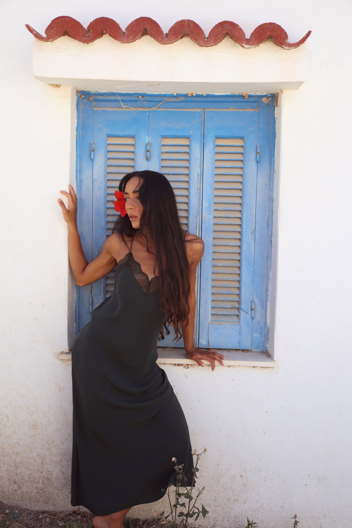 Freya Silk Midi Slip Dress in Forest Green - model posing against blue shuttered window showing relaxed slip silhouette - Lilly Pilly Collection