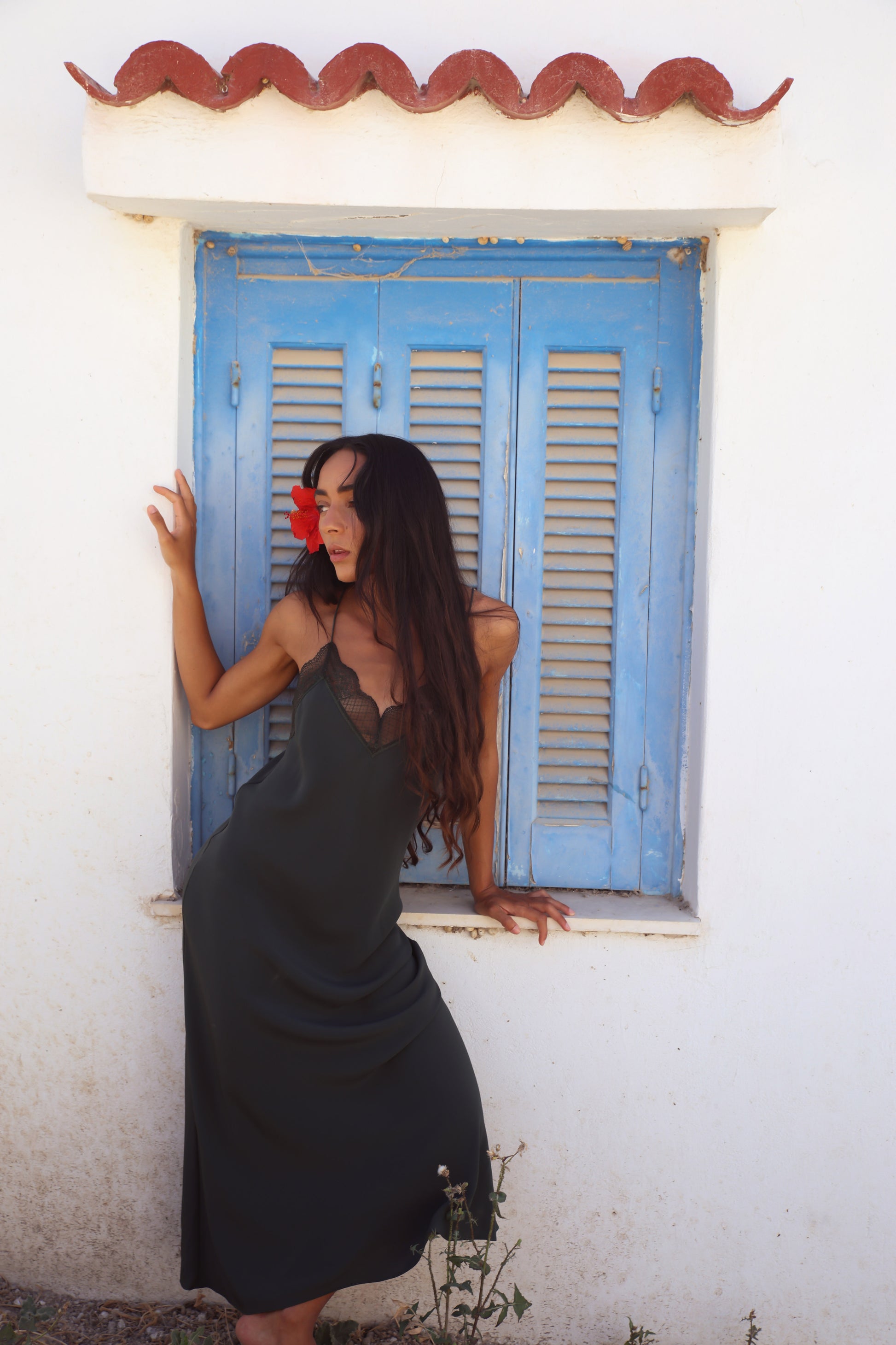 Freya Silk Midi Slip Dress in Forest Green - model posing against blue shuttered window showing relaxed slip silhouette - Lilly Pilly Collection