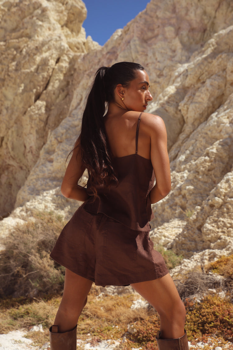 Gaia Linen Shorts in Chocolate - three-quarter view, woman wearing Chocolate linen shorts with matching chocolate linen cami, rocky outdoor backdrop - Lilly Pilly Collection