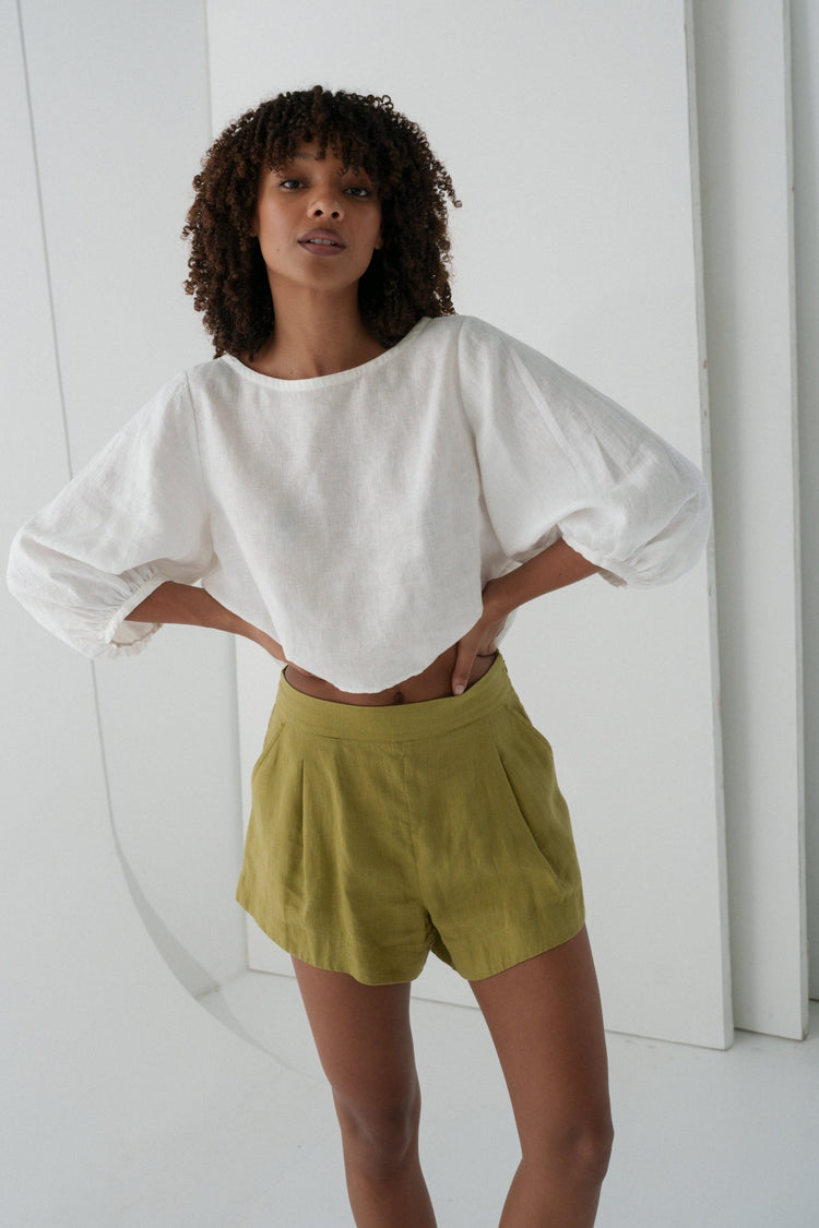Gaia Linen Shorts in Olive - full length front view, woman wearing Olive linen shorts with ivory linen puff-sleeve crop top, hands on hips, white studio backdrop - Lilly Pilly Collection