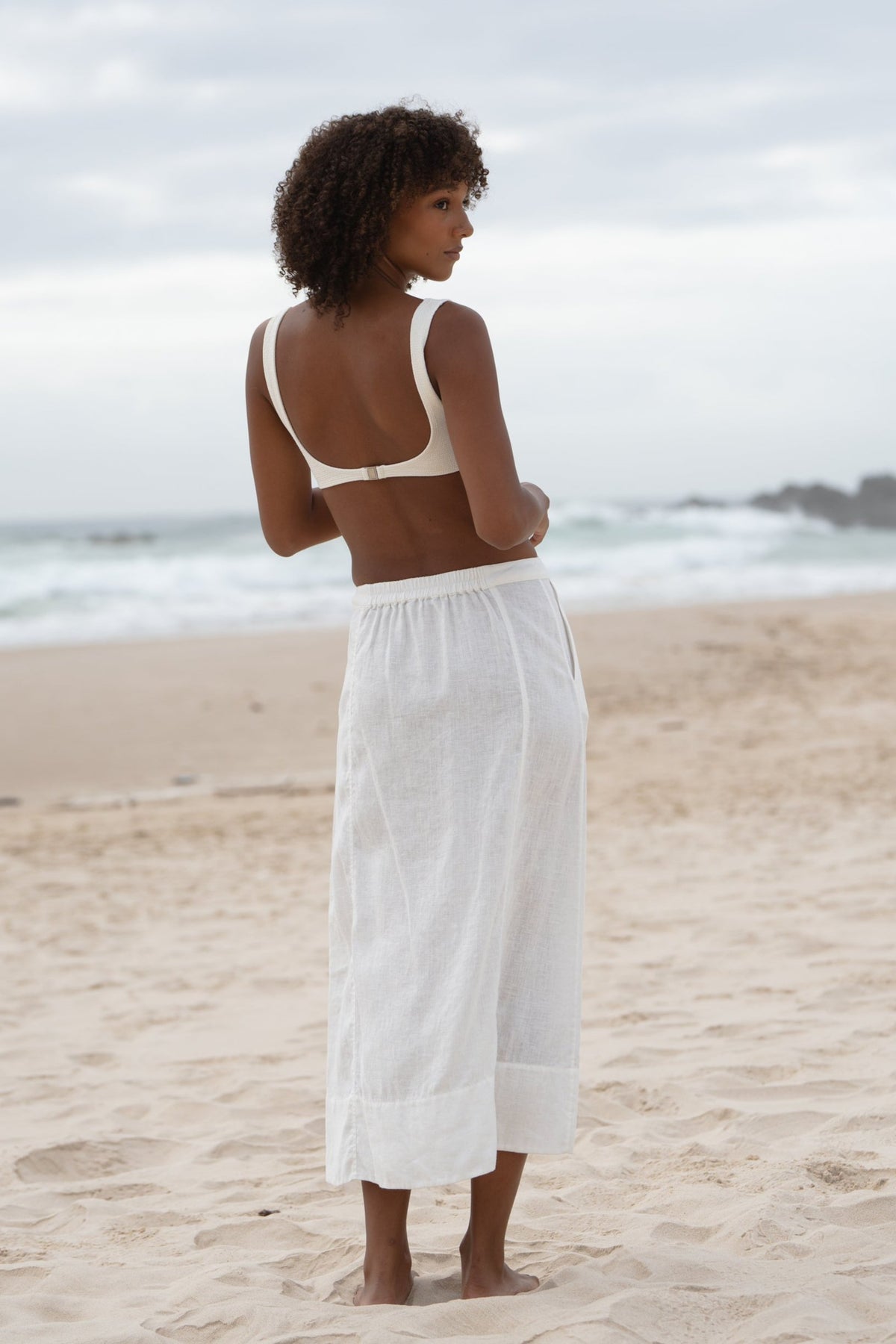 Woman wearing  a LILLY PILLY Gia linen skirt in Ivory showing back view while on the sandy beach