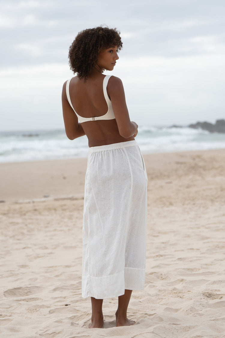 Gia Linen Midi Skirt in Ivory - back view, elasticated waistband, worn with square-neck bralette, standing on beach - Lilly Pilly Collection