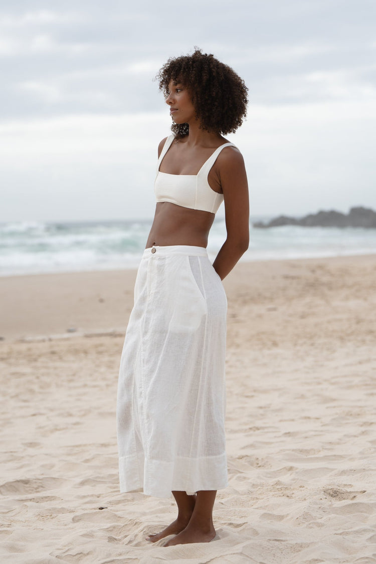 Gia Linen Midi Skirt in Ivory - side profile, elasticated waist, worn with square-neck bralette, standing on beach - Lilly Pilly Collection