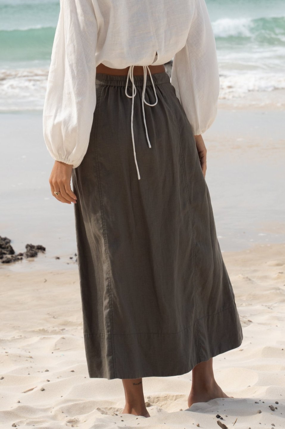 Close up view of LILLY PILLY Gia linen skirt in Khaki on the beach showing back view