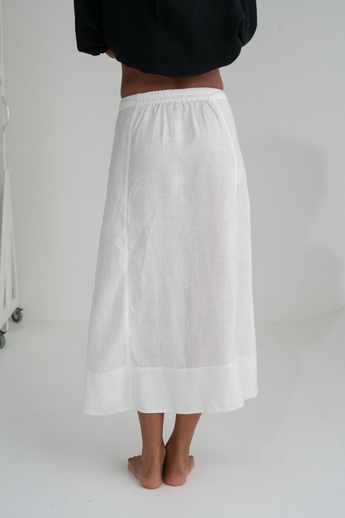 Back view of  woman wearing an ivory white Gia linen skirt worn by a person on a plain background